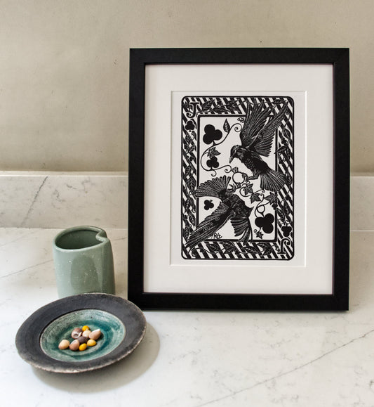 Framed artwork with a black and white design of birds and floral elements on a white surface.