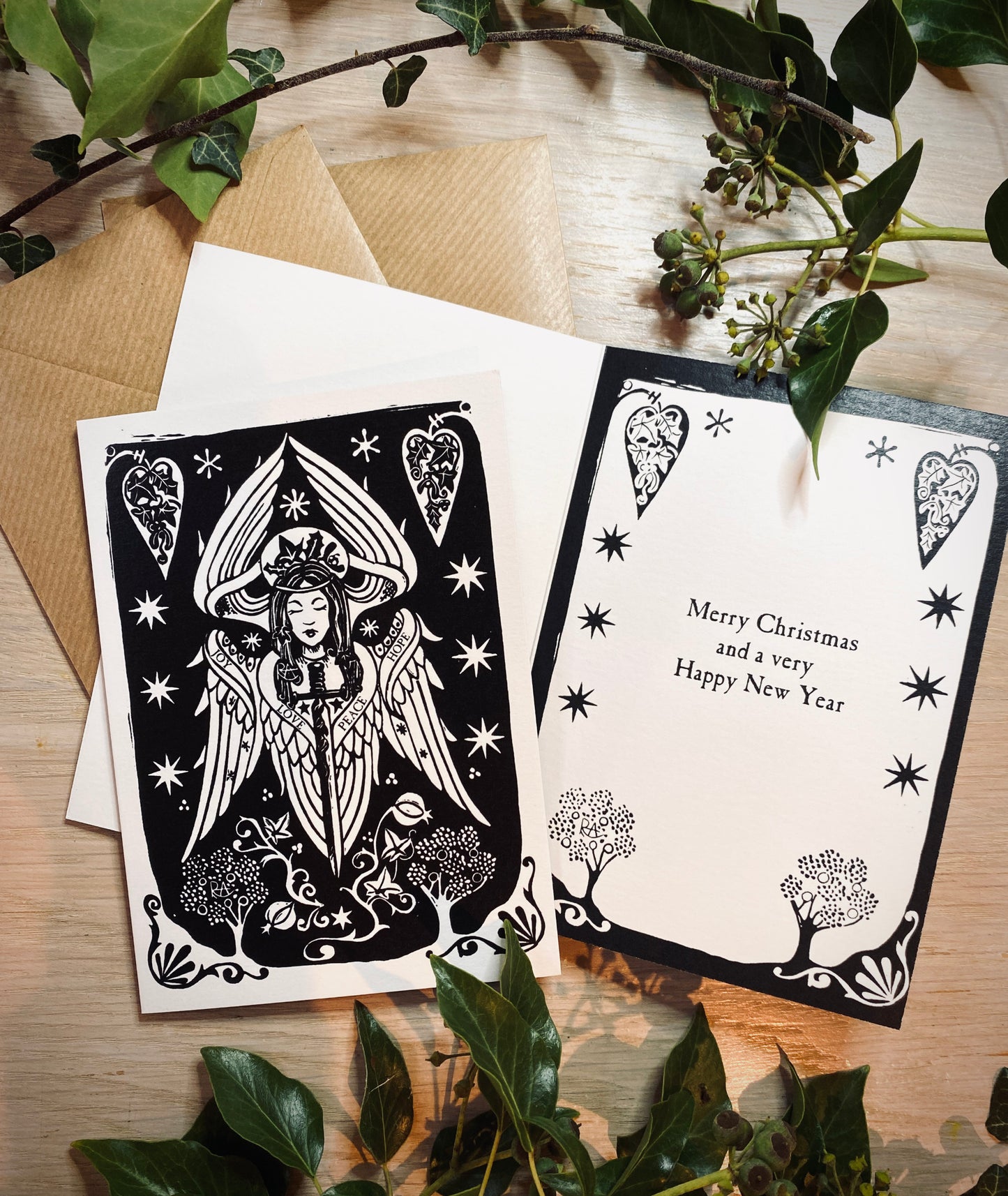 Angel greeting cards with decorative designs on a wooden surface with greenery.