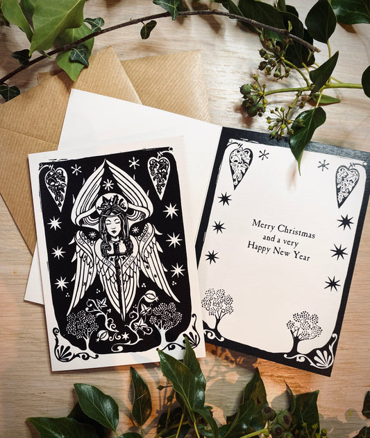 Angel greeting cards with decorative designs on a wooden surface with greenery.