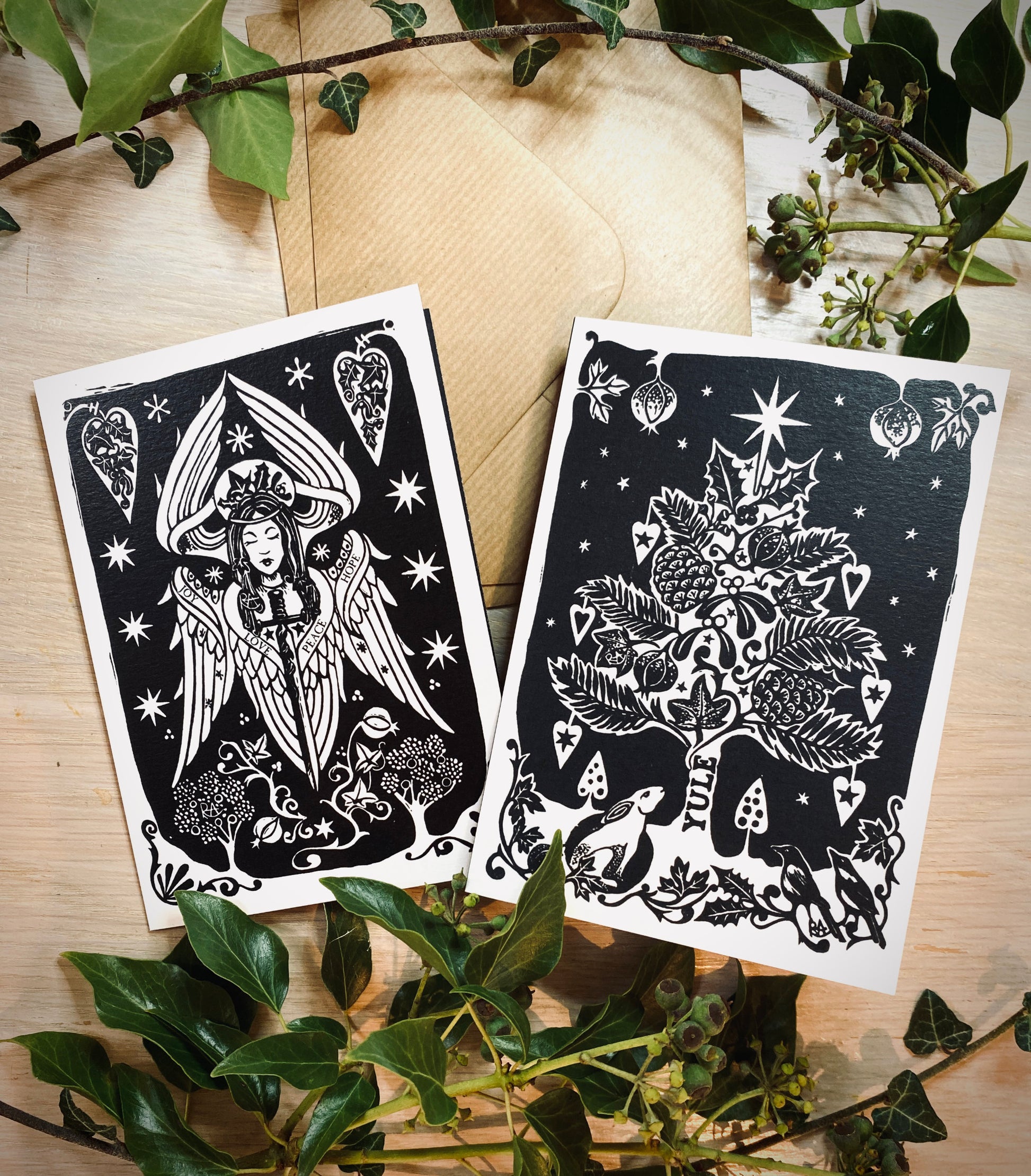 Two black and white illustrated cards on a wooden surface with green leaves.