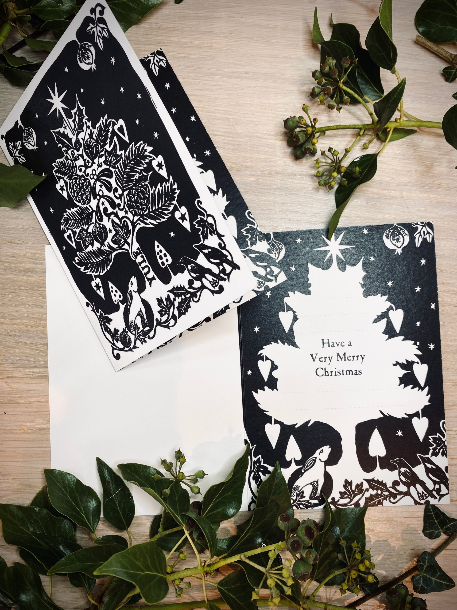 Black and white Christmas cards with festive designs on a wooden surface with greenery.