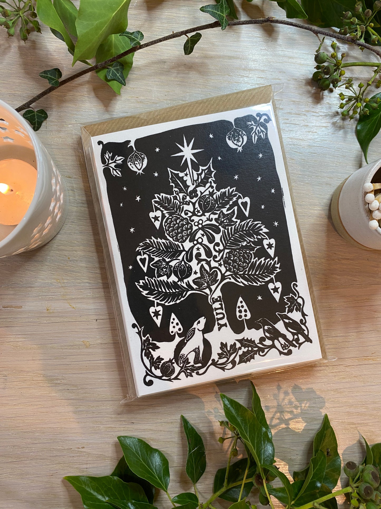 Decorative card with black and white design on a wooden surface with candles and plants.