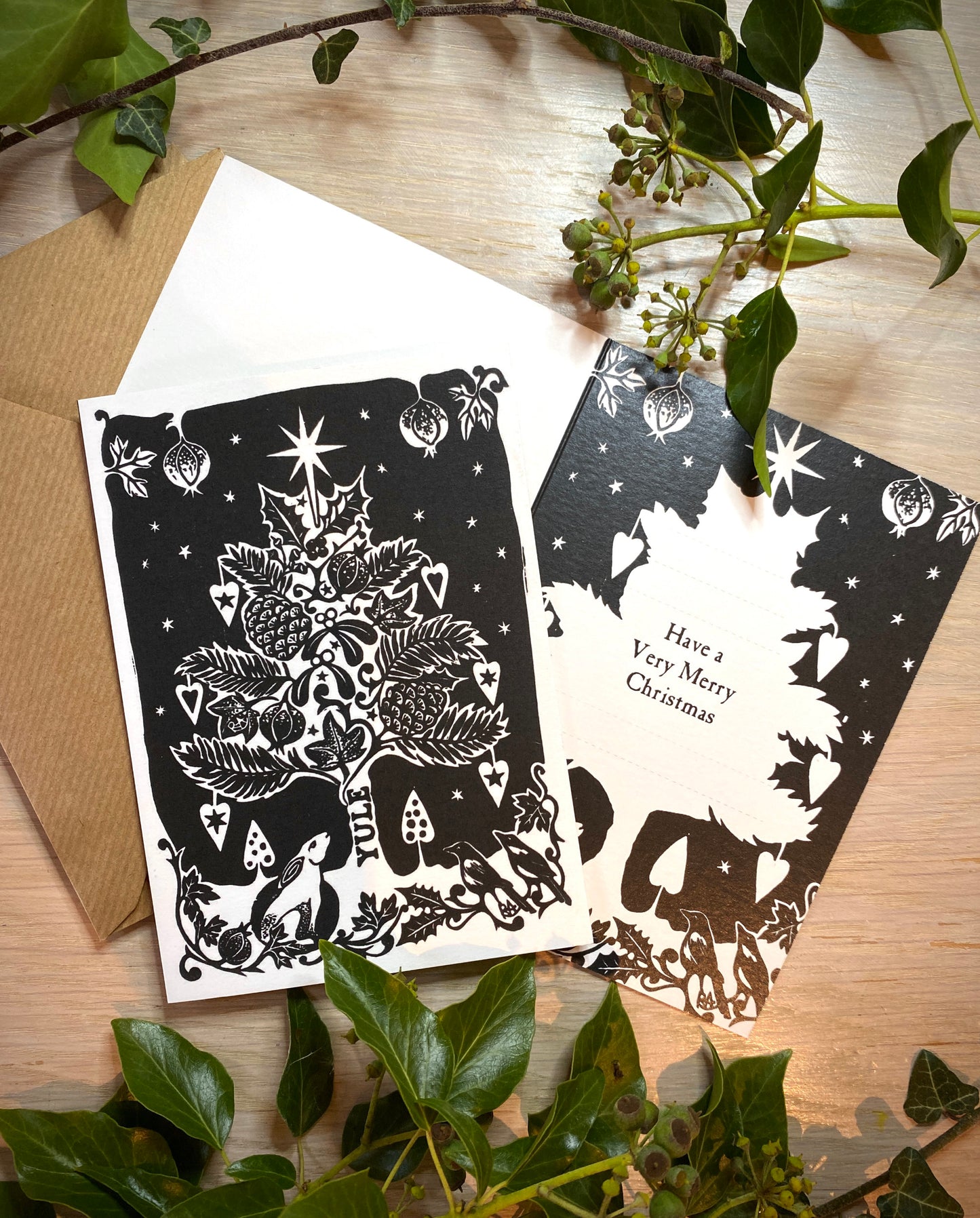 Two black and white Christmas cards with decorative elements on a wooden surface.