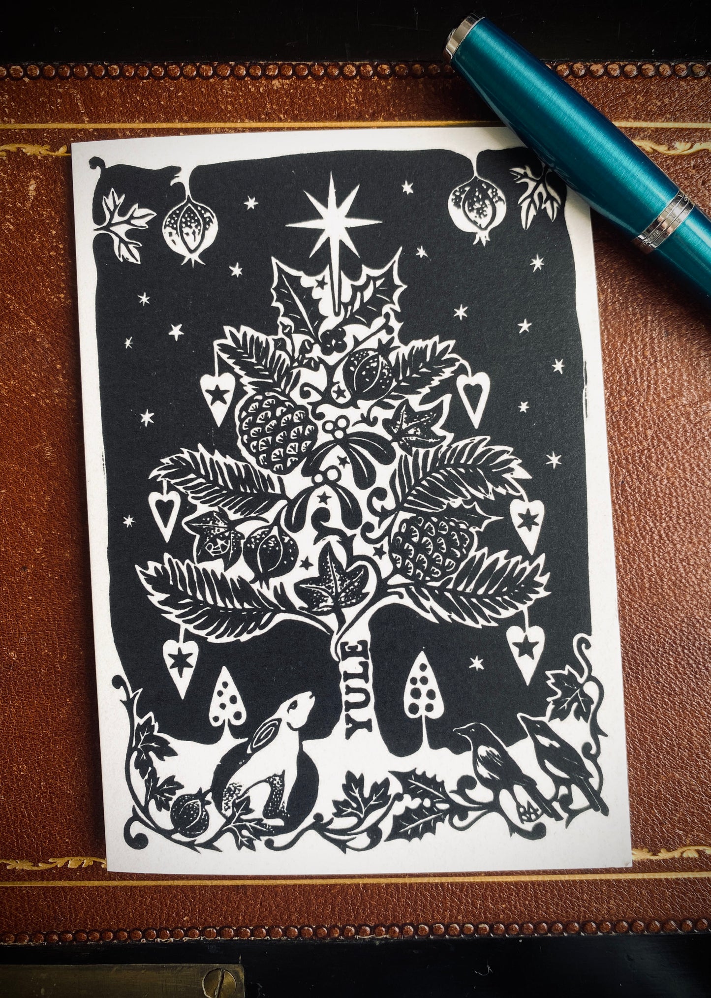Decorative Christmas tree design on a piece of paper with a pen on a brown surface.