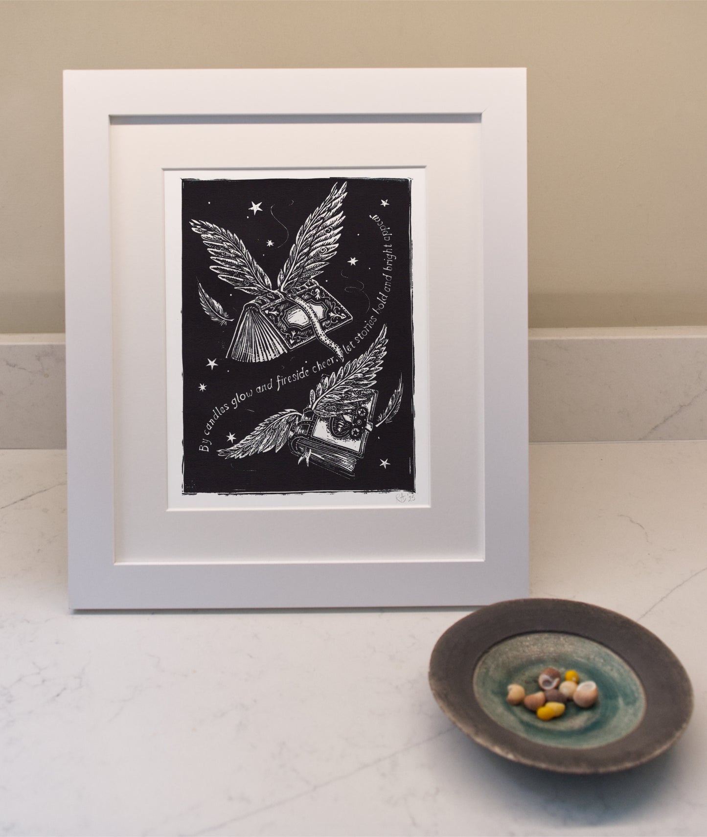 Framed artwork with a black background and white border, featuring wings and text, on a light surface.