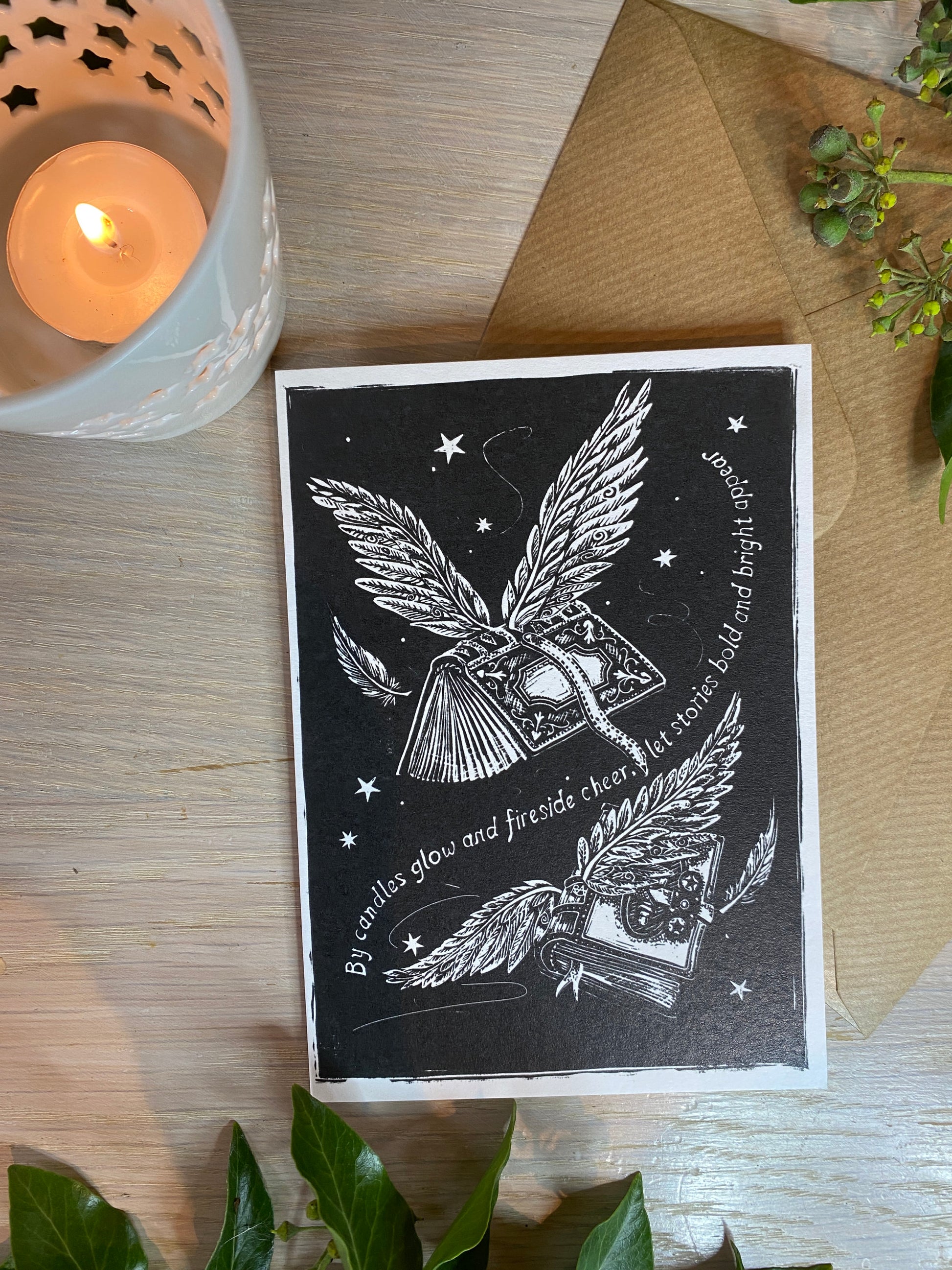 Black and white illustration of a winged book with text on a wooden surface with a candle.