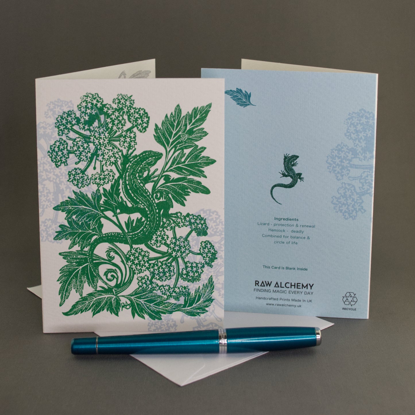 Greeting card with green lizard and foliage design, blue pen, and another card with a lizard illustration on a dark background.