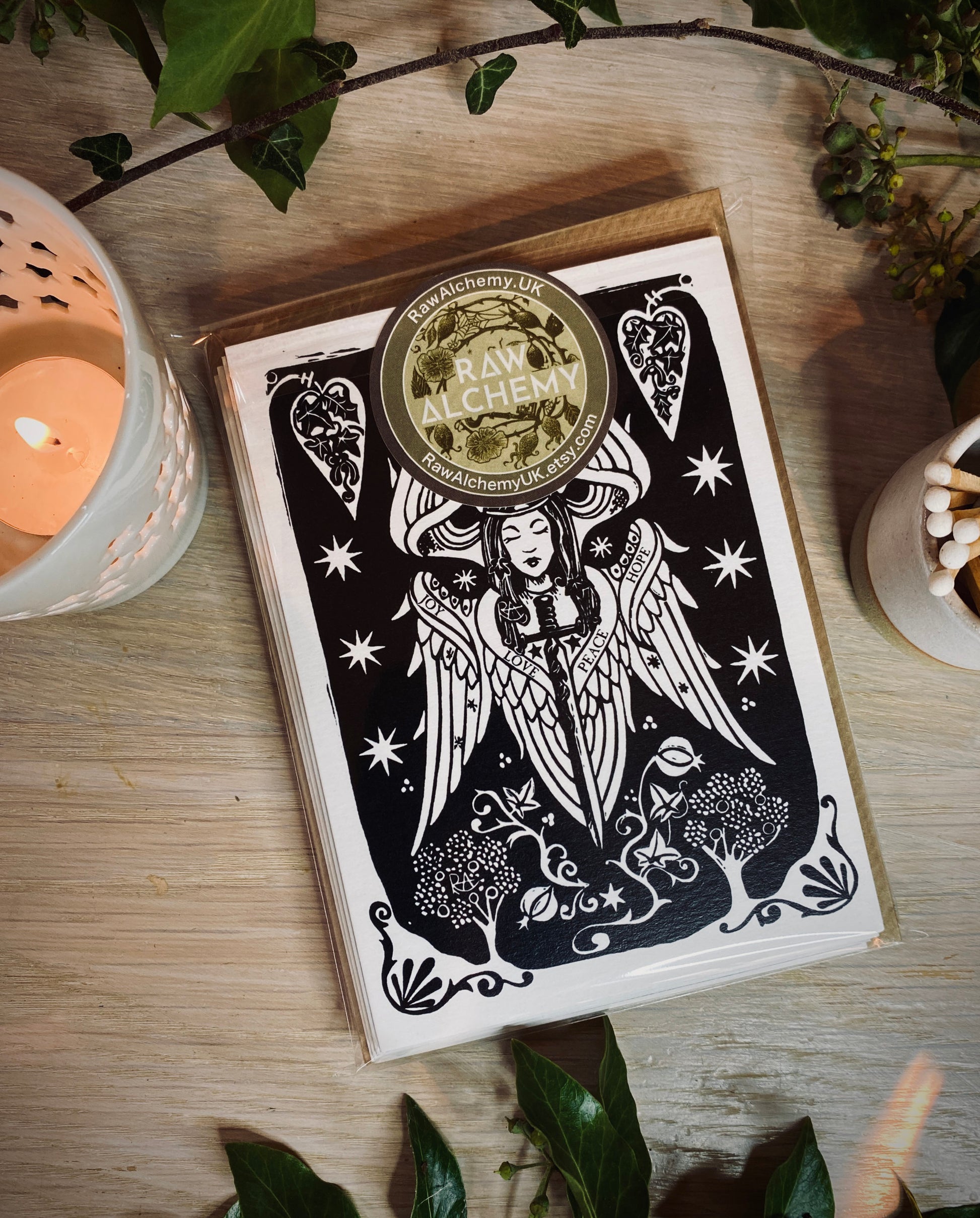 Card pack with black and white illustration on a wooden surface with a candle and plants.