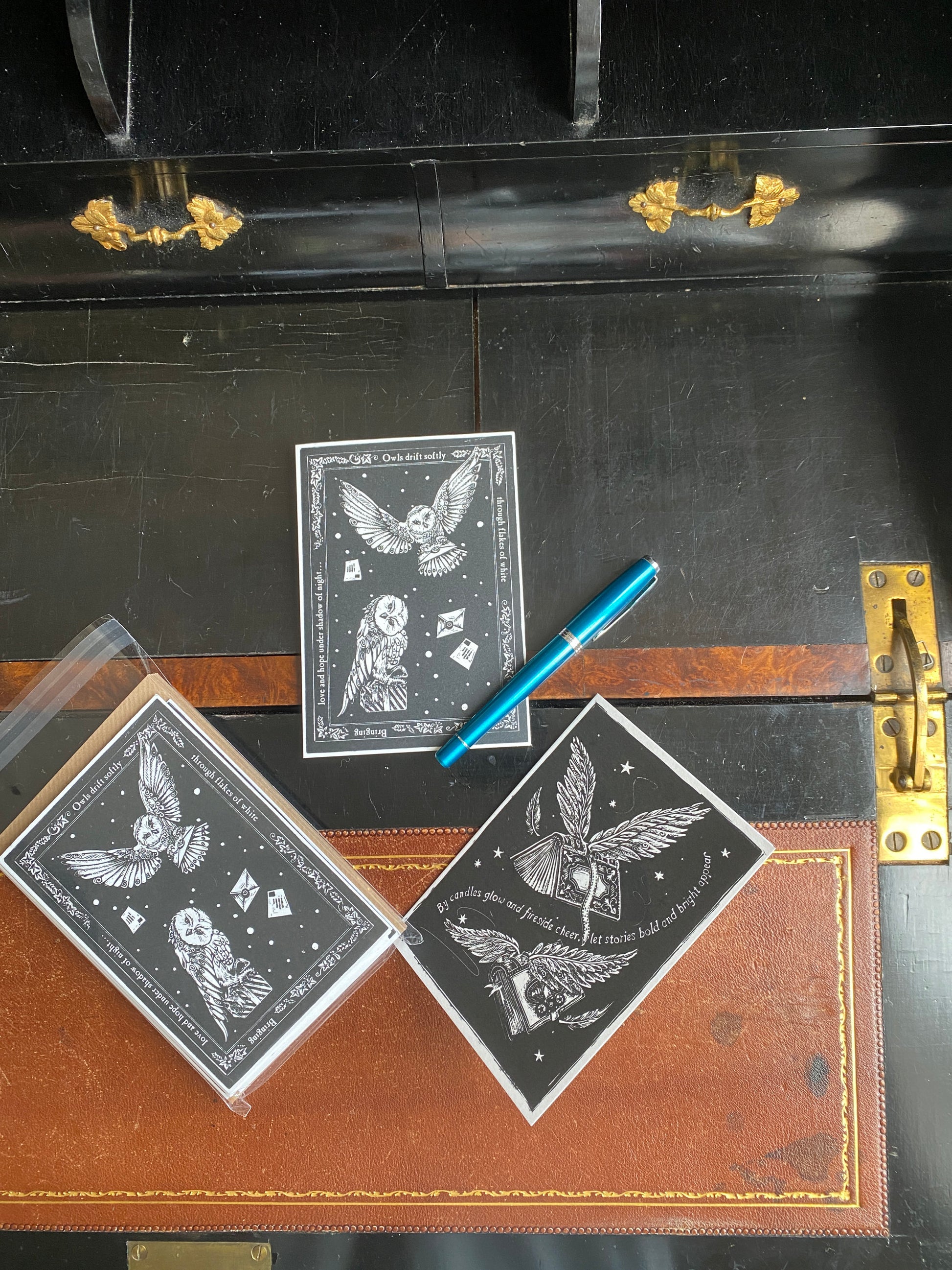 Three christmas cards with owl designs on a dark surface next to a pen.
