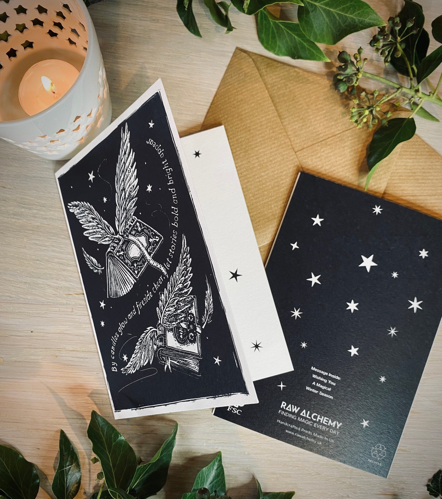 Two black and white cards with star and wing designs on a wooden surface with a candle and leaves.