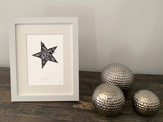 Framed artwork with a star design on a wooden surface with decorative metallic balls.