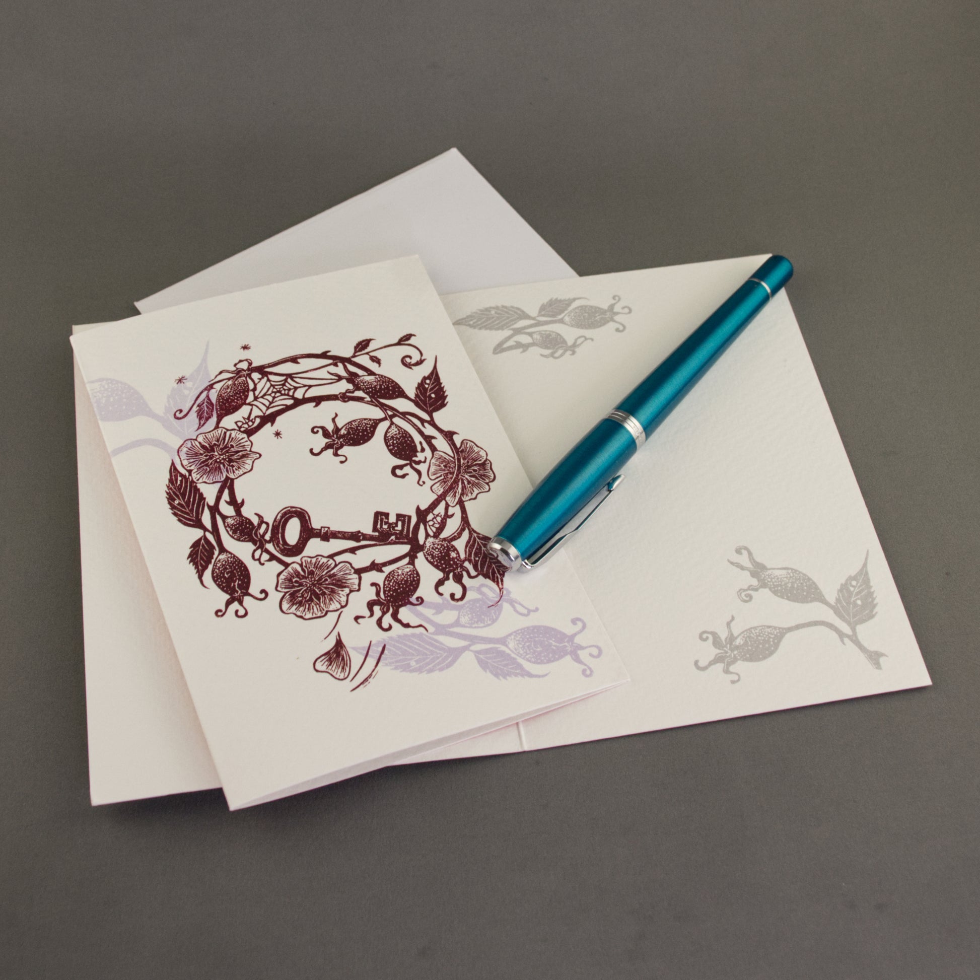 Greeting card with floral design, blue pen, and matching envelope on a gray background
