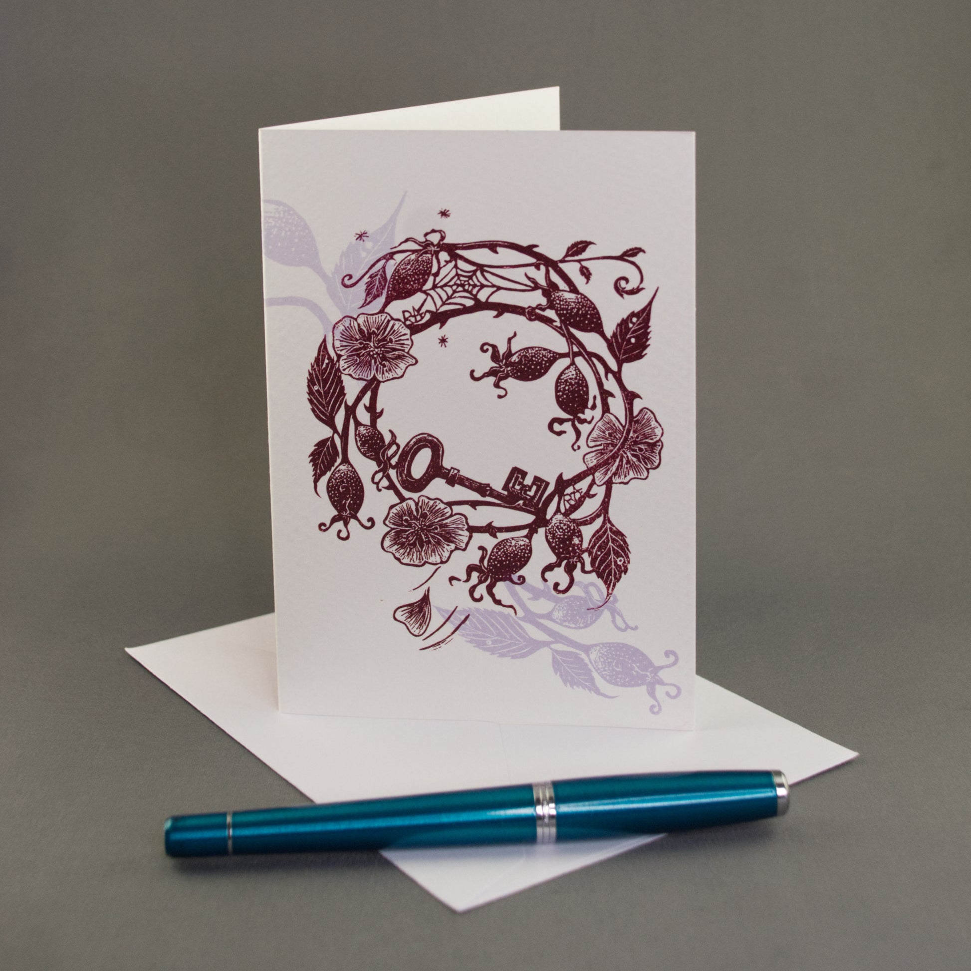 Greeting card with floral design on a gray background with a blue pen.
