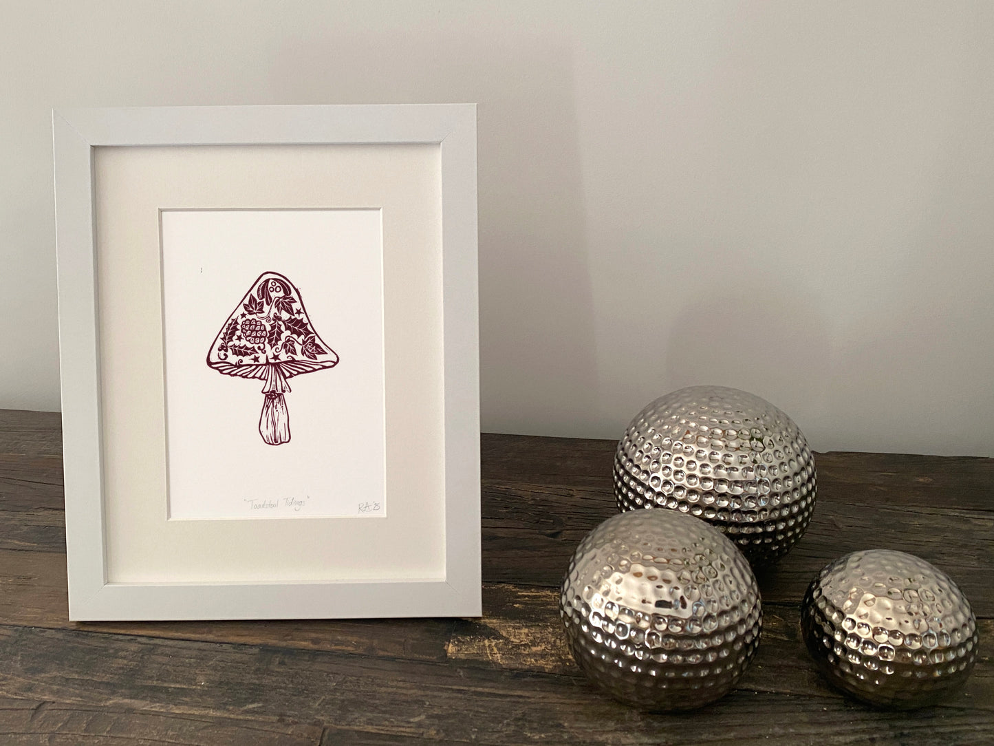Framed artwork of a mushroom on a wooden surface with decorative metallic balls.