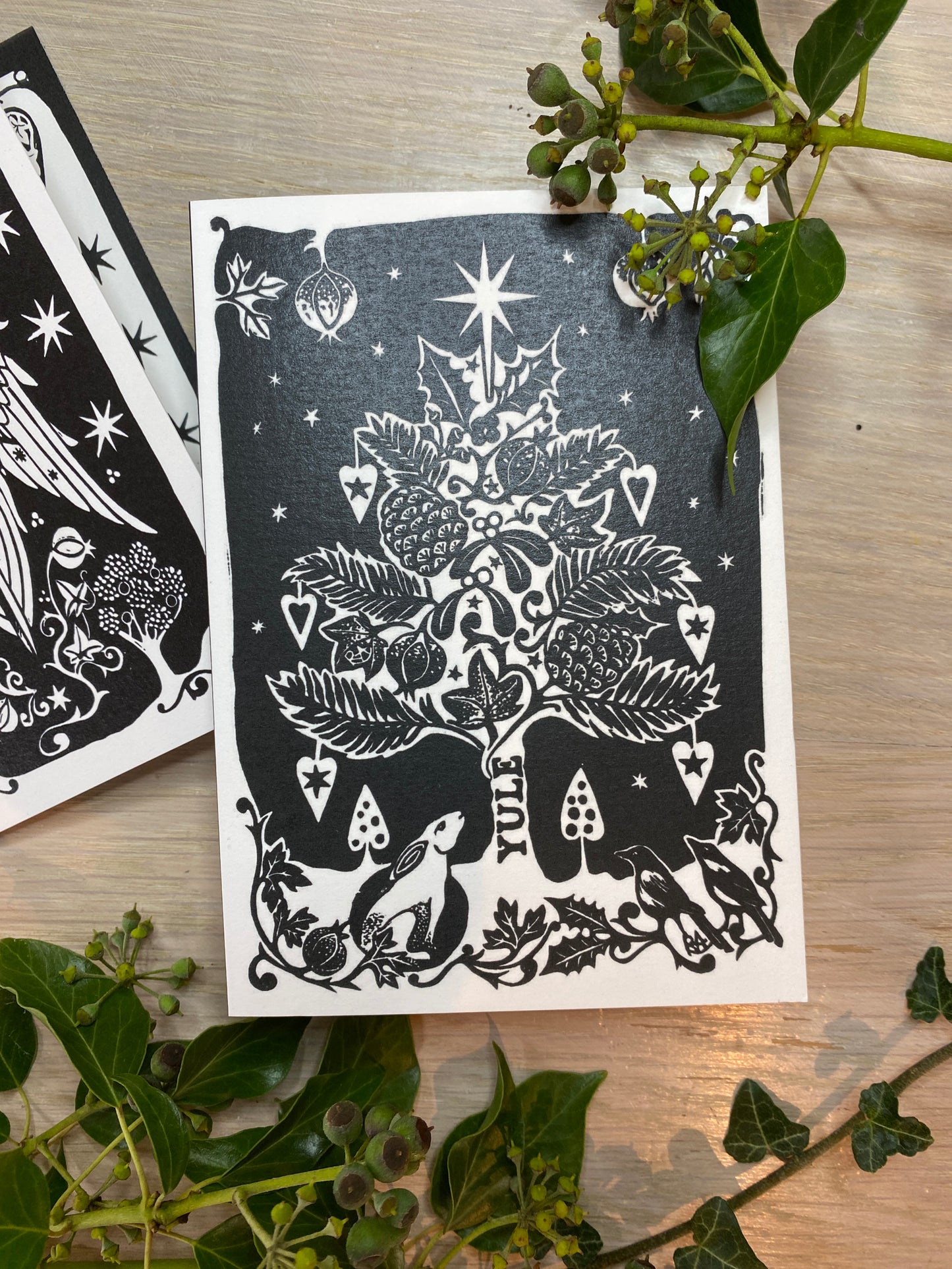 Black and white illustration of a tree and animals on a card with green leaves around.