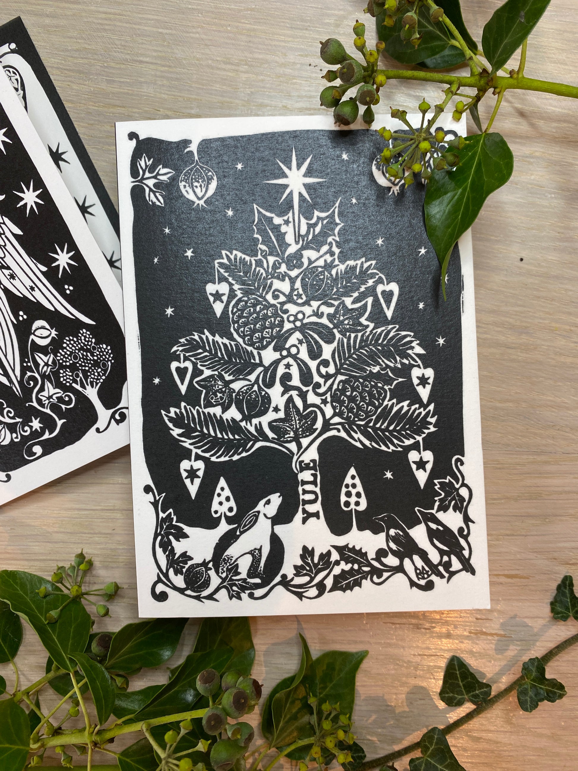 Black and white illustration of a tree and animals on a card with green leaves around.
