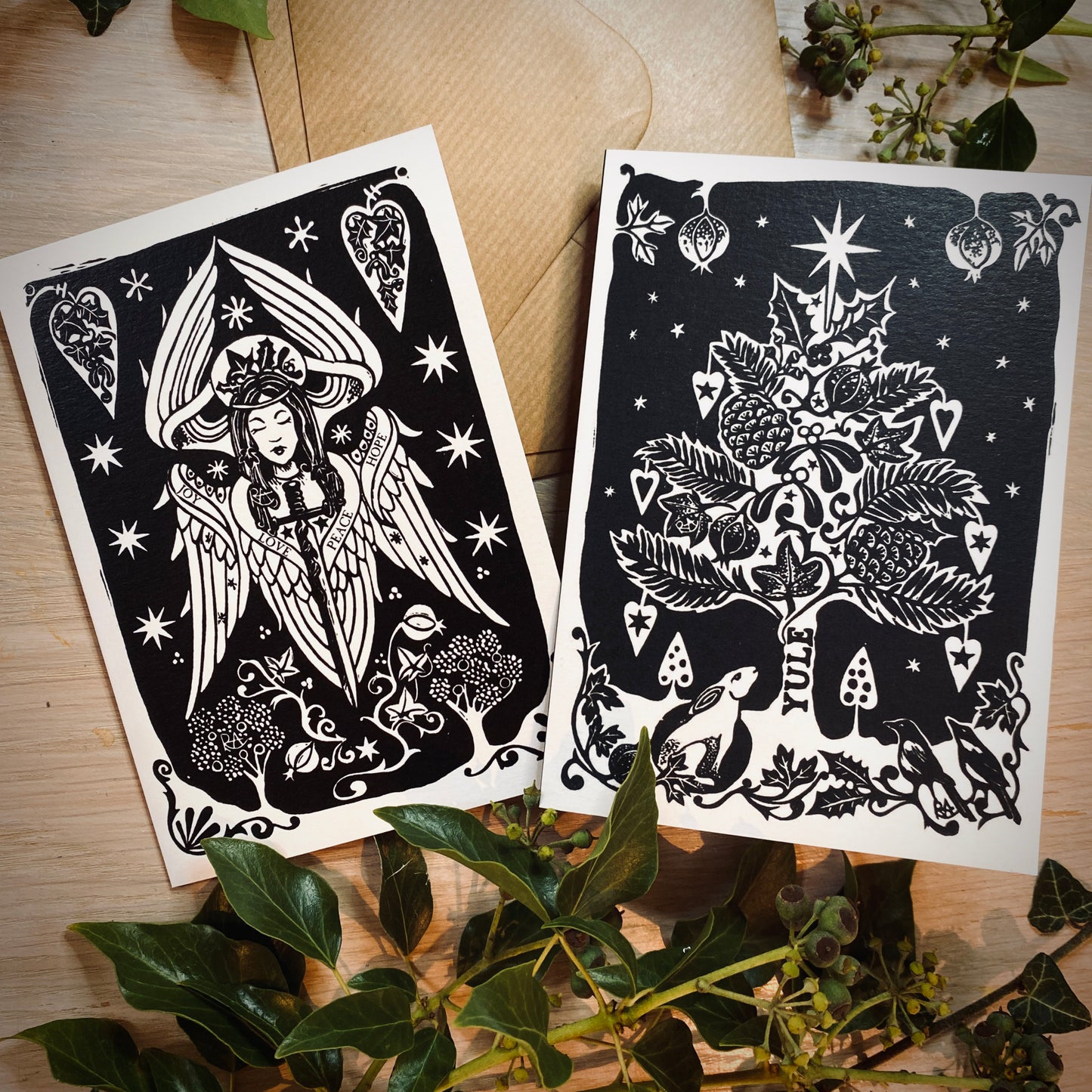 Two black and white christmas cards on paper with decorative elements on a wooden surface.