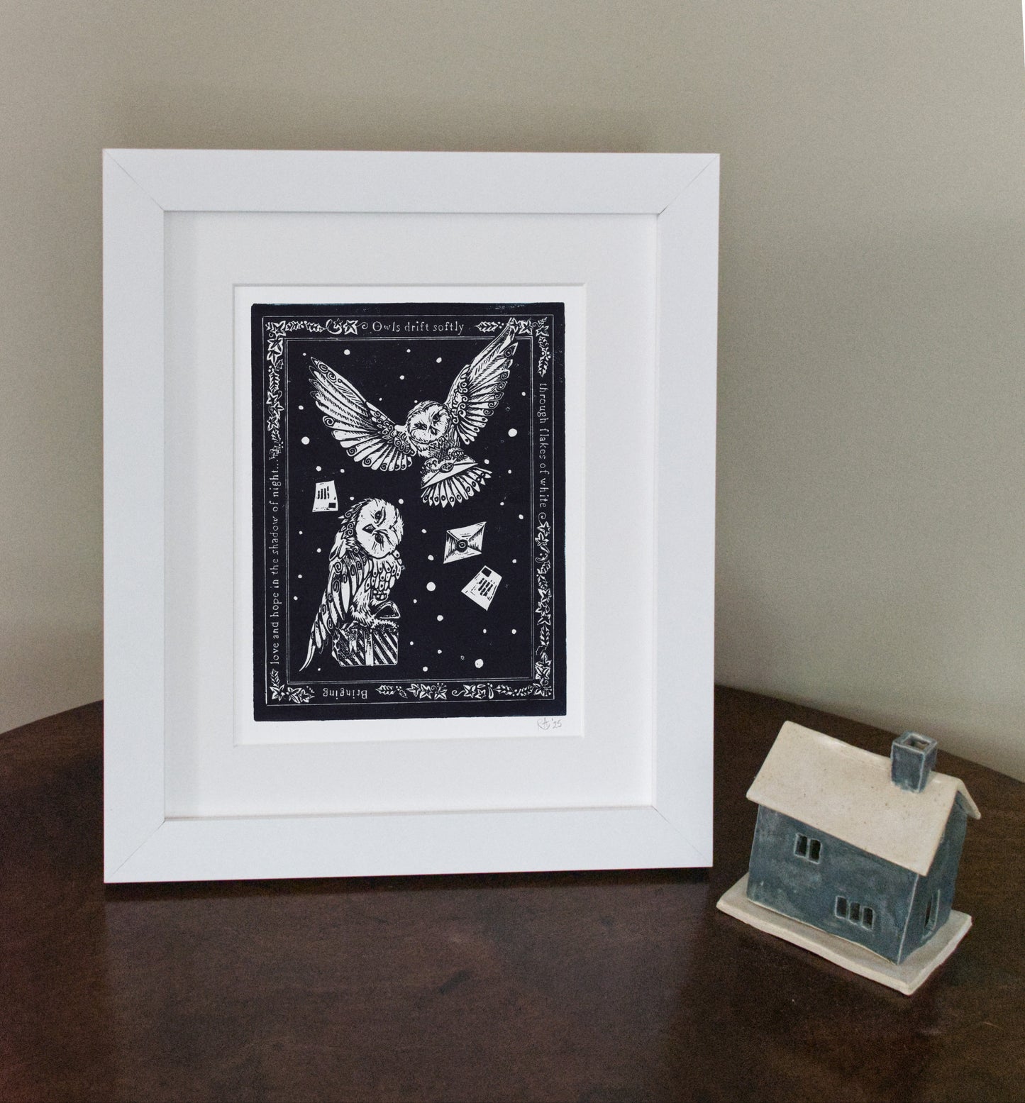 Framed artwork with an owl design on a dark background, placed on a wooden surface.
