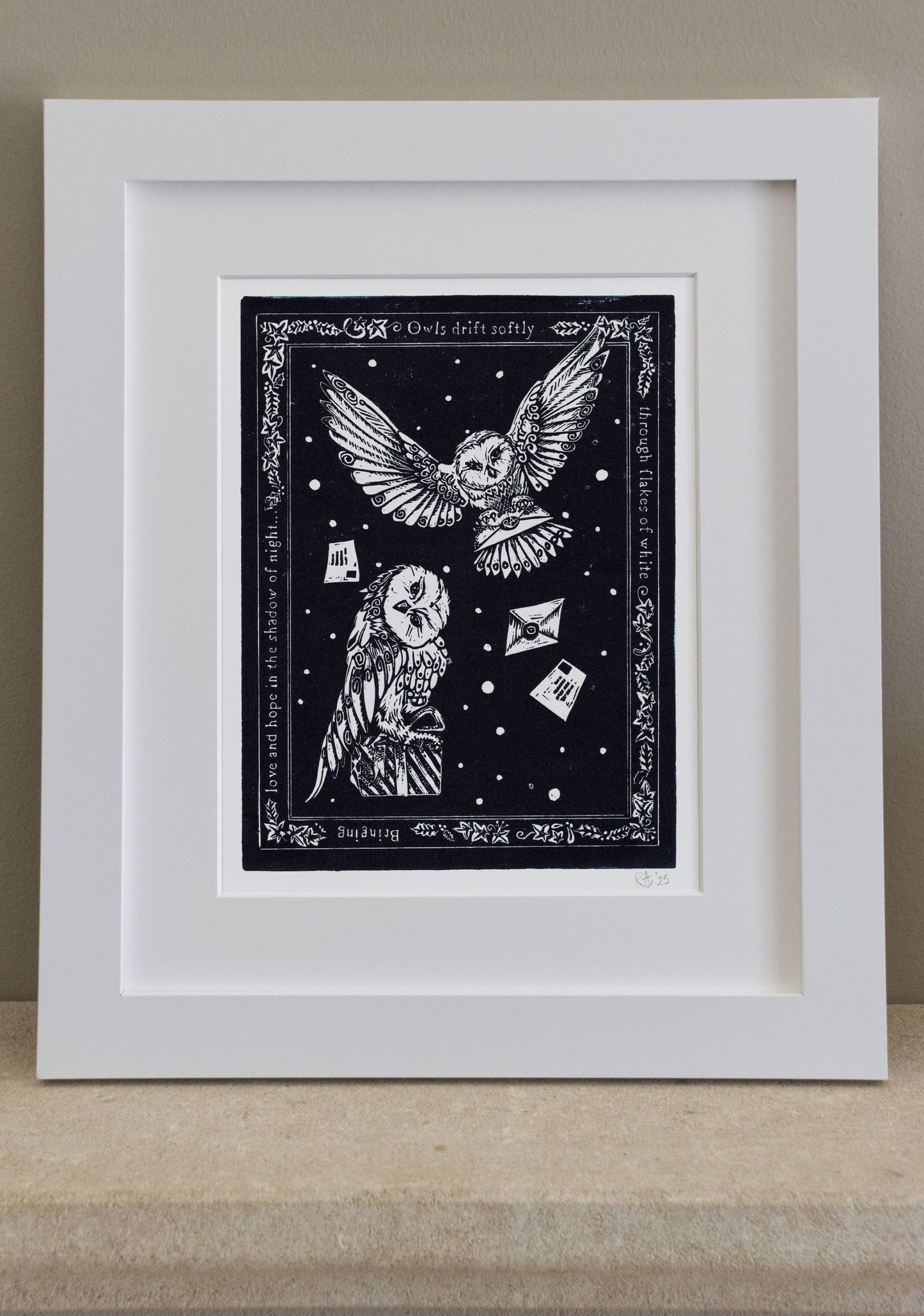 Framed artwork with an owl design on a black background, displayed on a wooden surface.