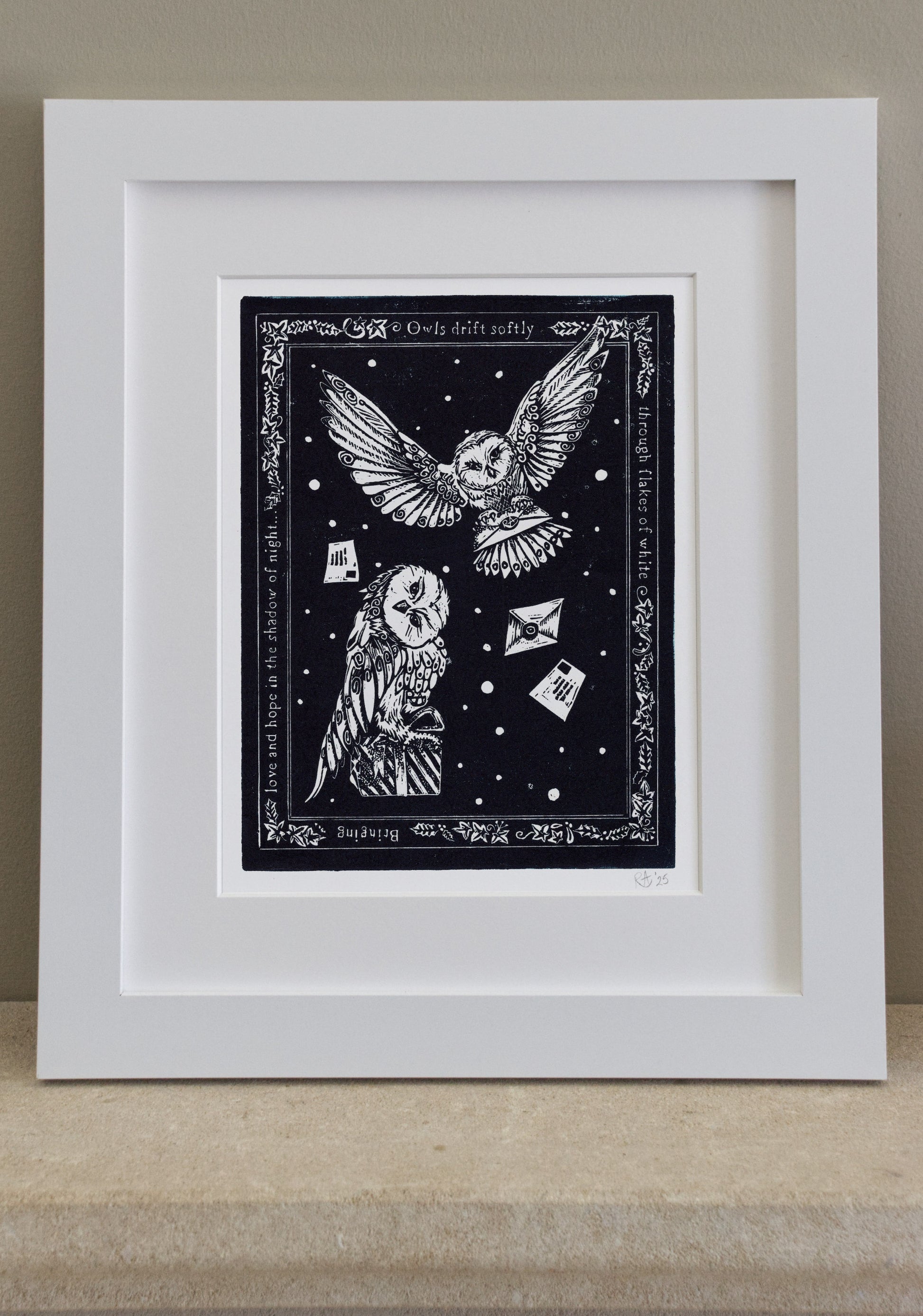 Framed artwork with an owl design on a black background, displayed on a wooden surface.