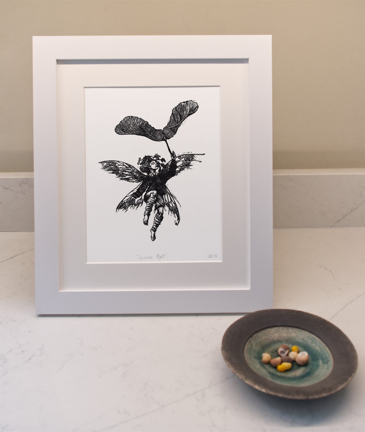 Framed black and white illustration of a fairy holding a leaf on a light surface with a bowl.