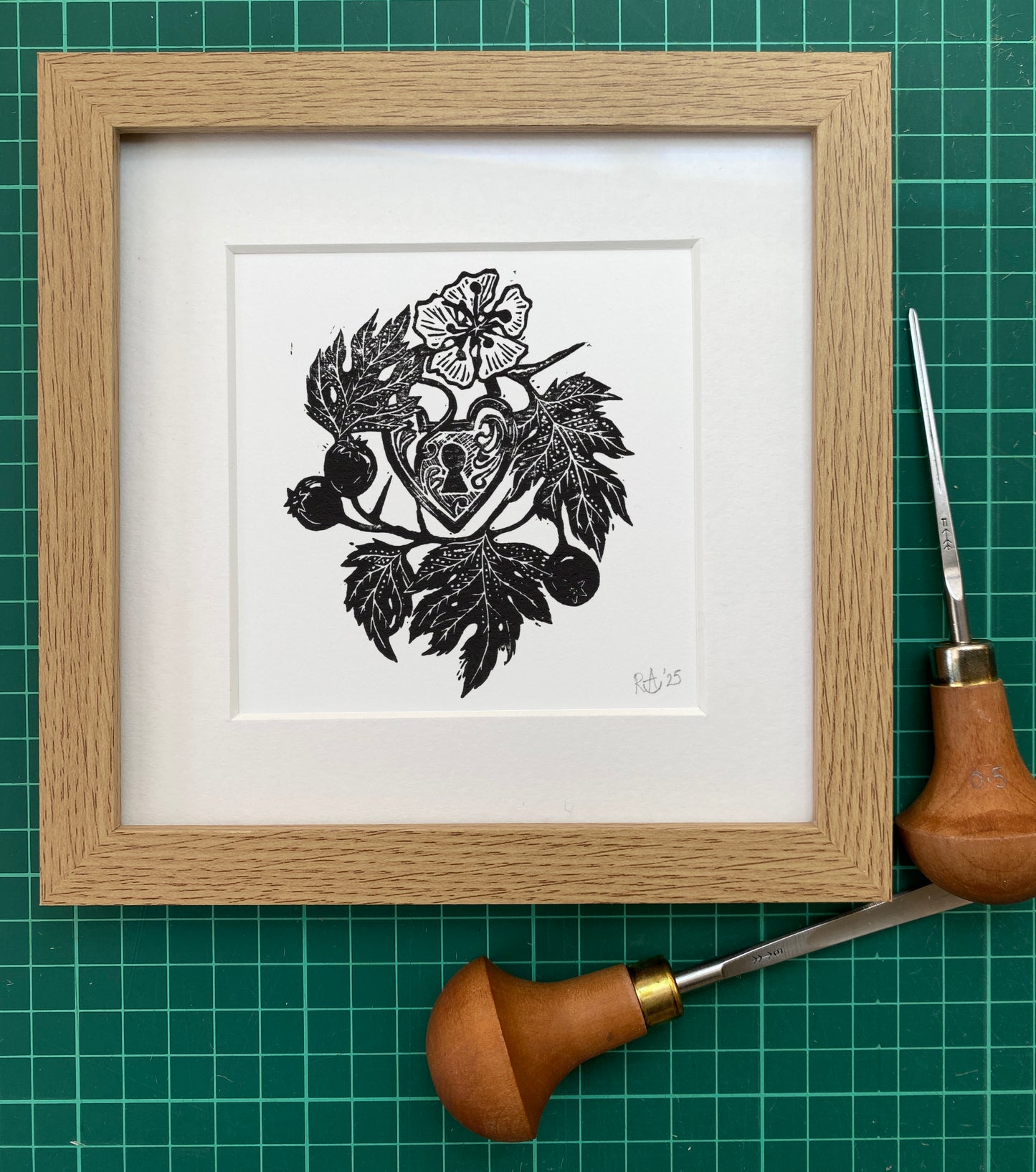 Framed black and white artwork on a green grid background with carving tools.