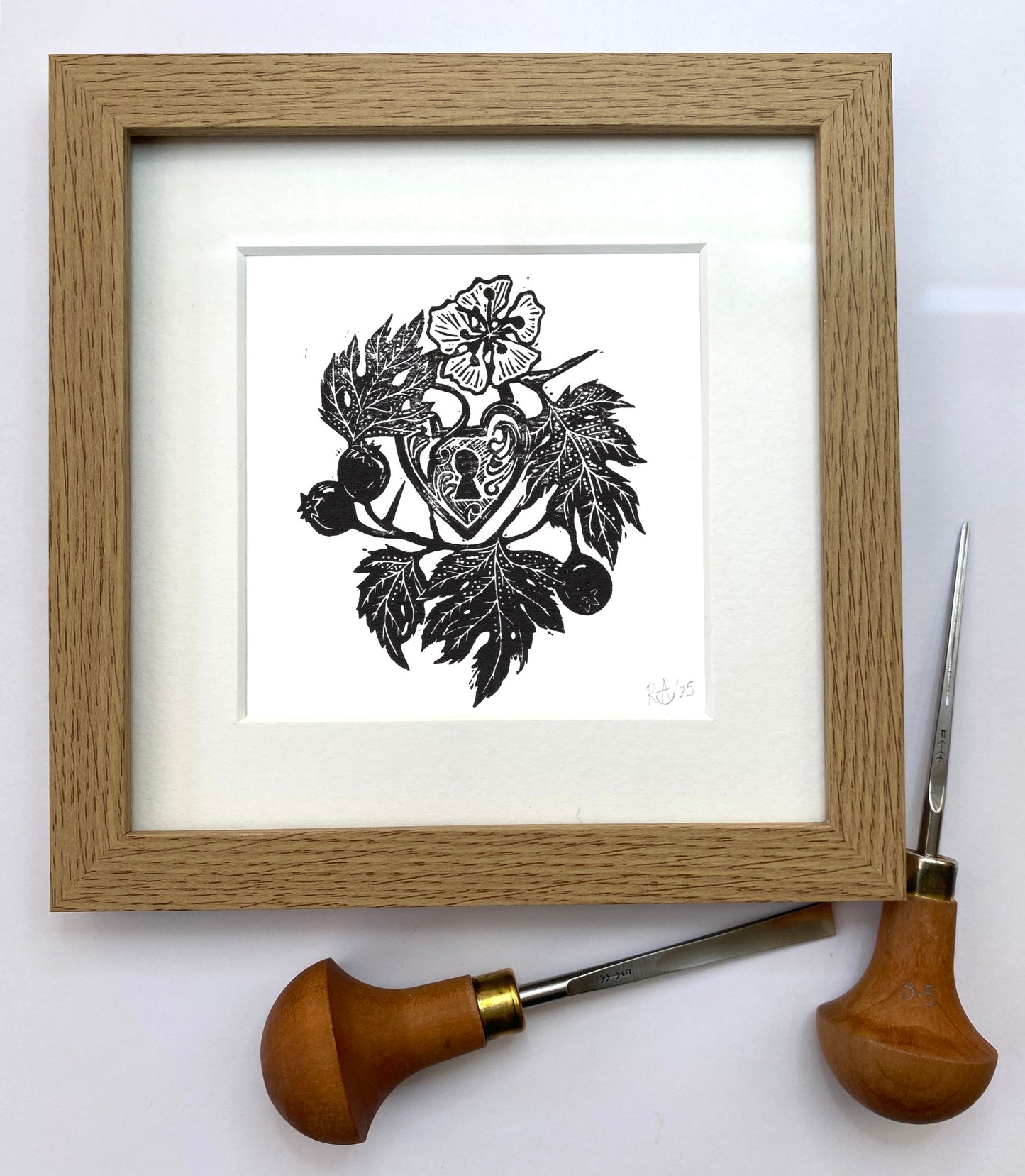 Framed black and white illustration of a heart with floral elements on a white background, with a woodcarving tool next to it.
