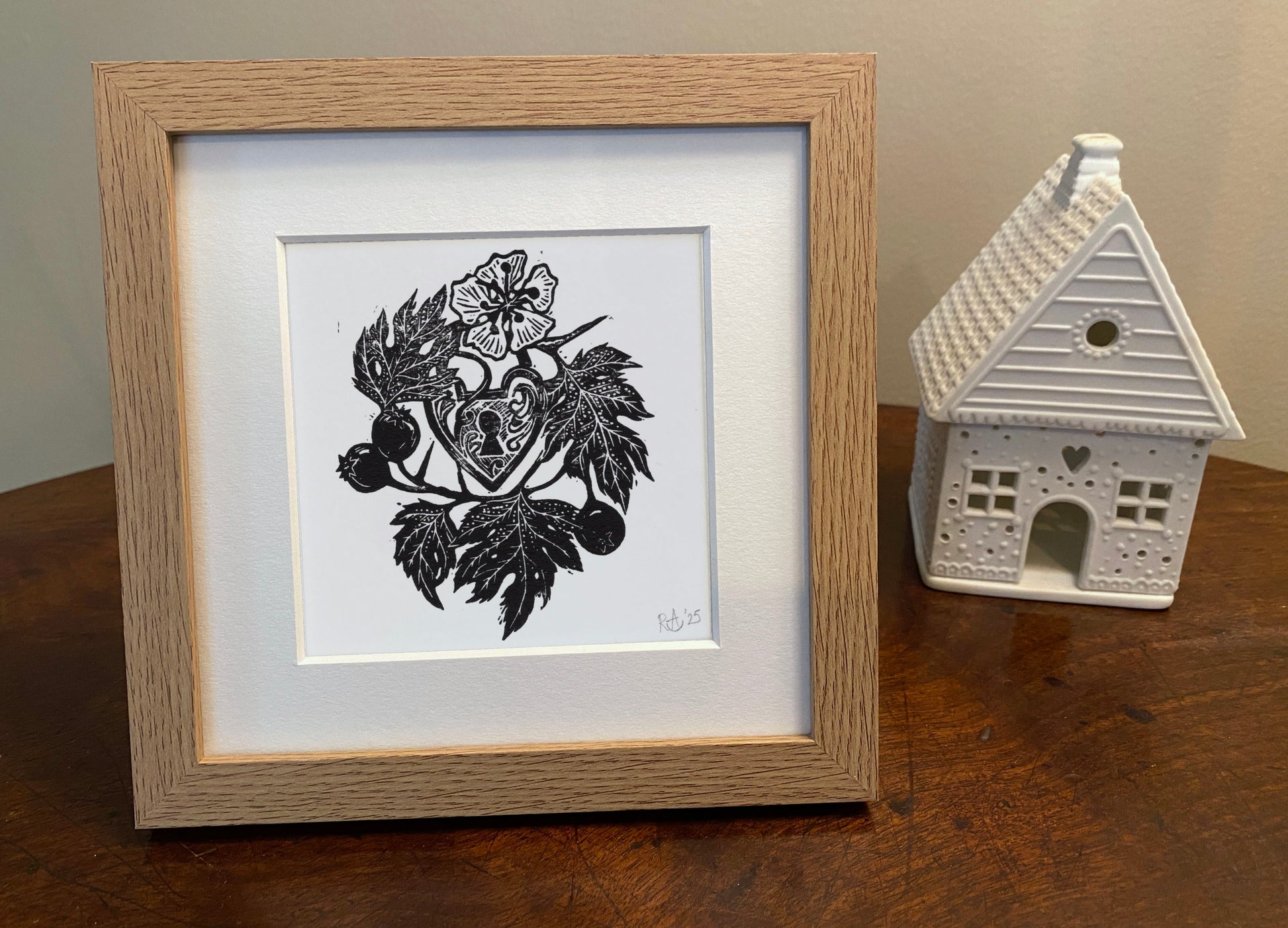 Framed black and white artwork on a wooden surface with a small decorative house.