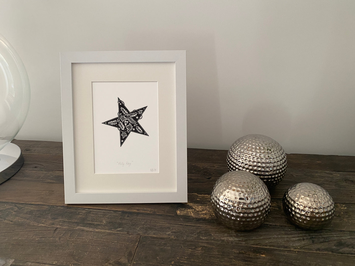 Framed artwork with a star design on a wooden surface next to decorative metallic balls.