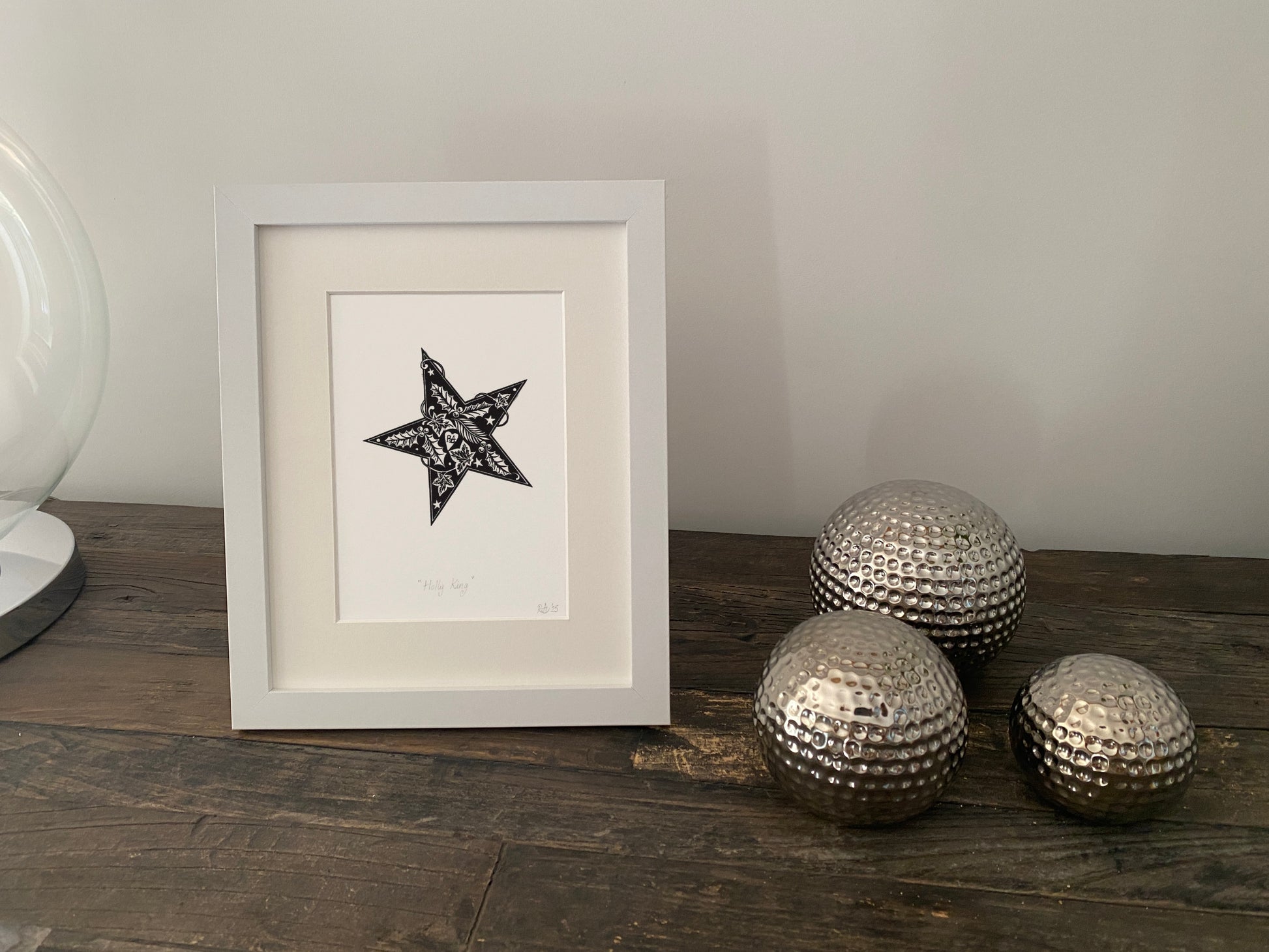 Framed artwork with a star design on a wooden surface next to decorative metallic balls.