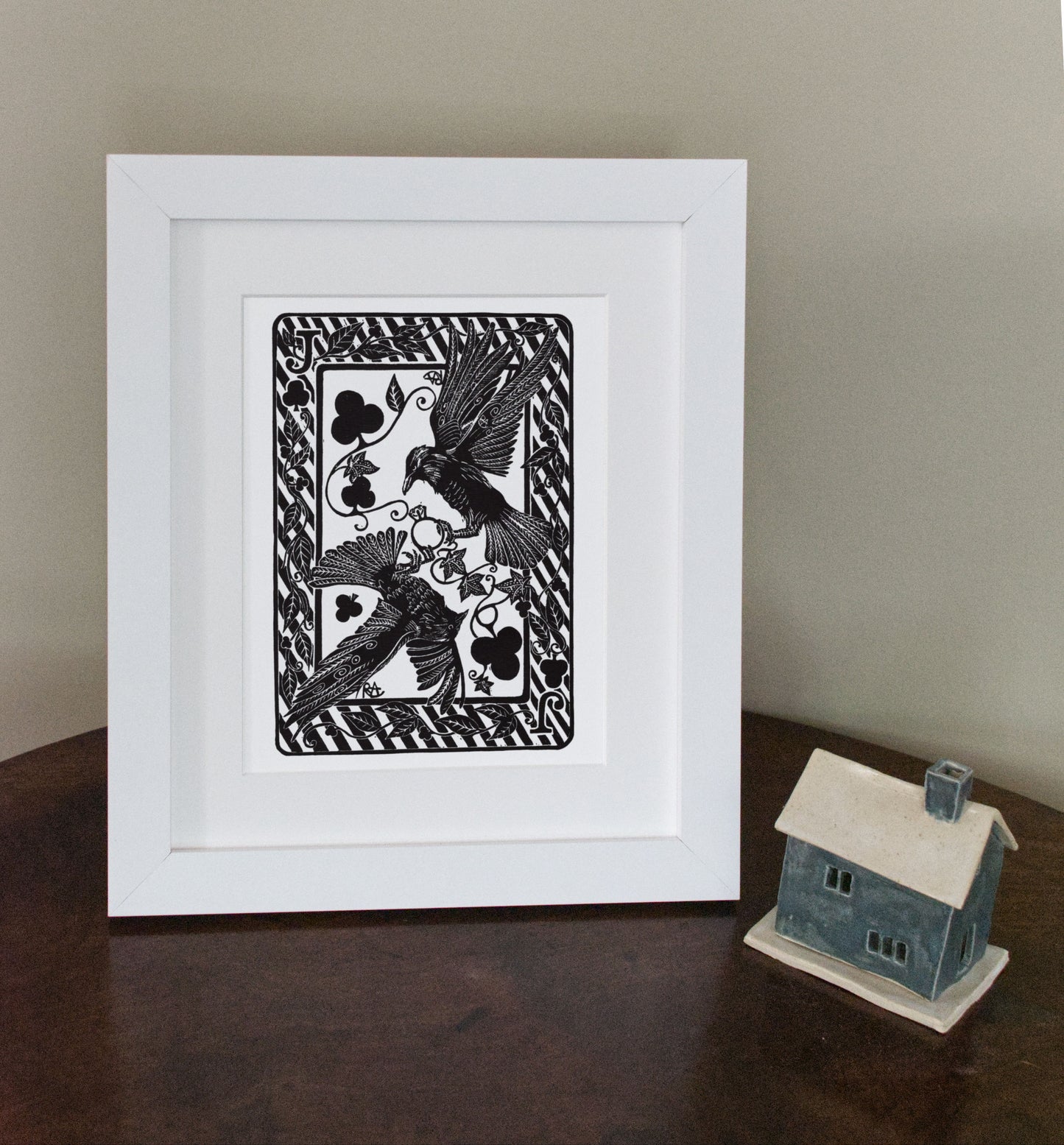 Framed black and white artwork of a bird with playing card symbols on a wooden surface.