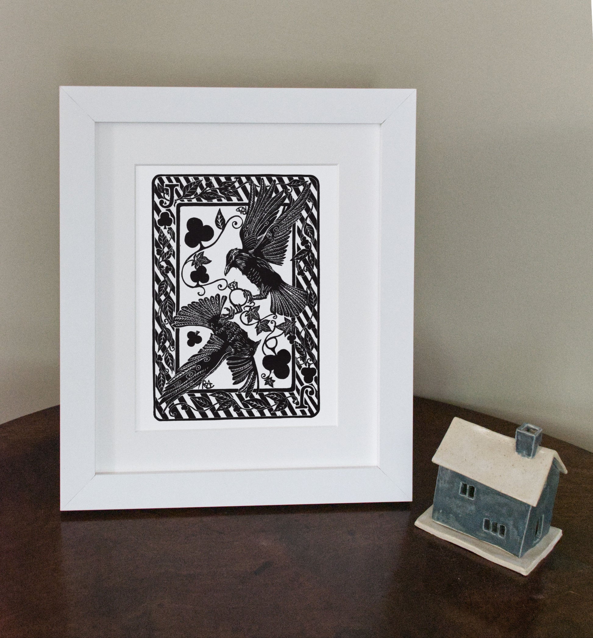 Framed black and white artwork of a bird with playing card symbols on a wooden surface.