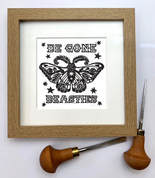 Framed artwork with a butterfly design and text 'Be Gone Beasties' on a white background, with a woodcarving tool beside it.