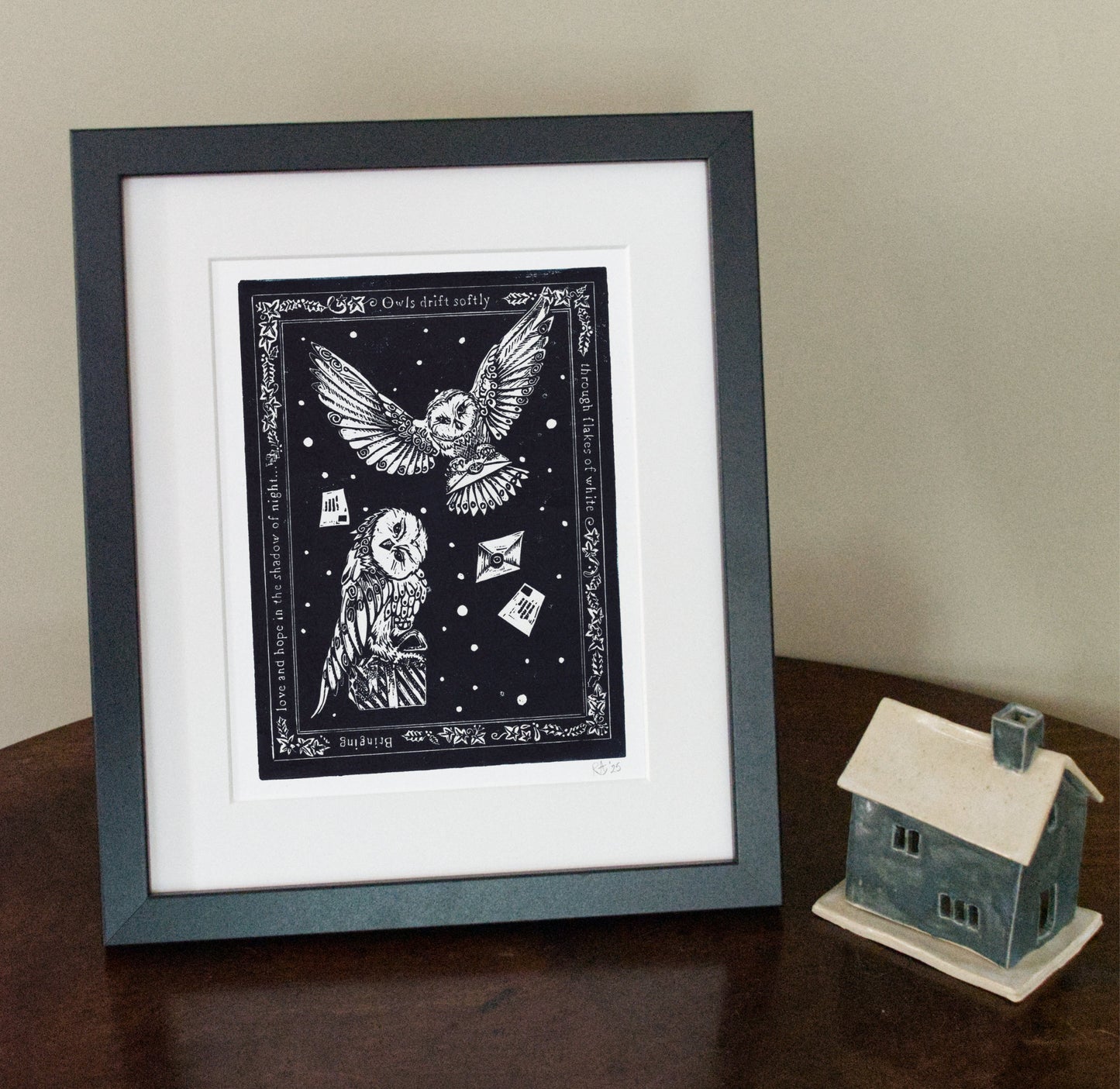 Framed black and white artwork of owls on a table with a small house model.
