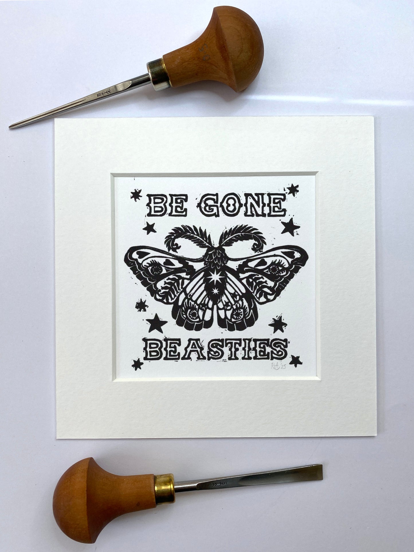 Print with butterfly design and text 'Be Gone Beasties' on a white background, surrounded by woodcarving tools.