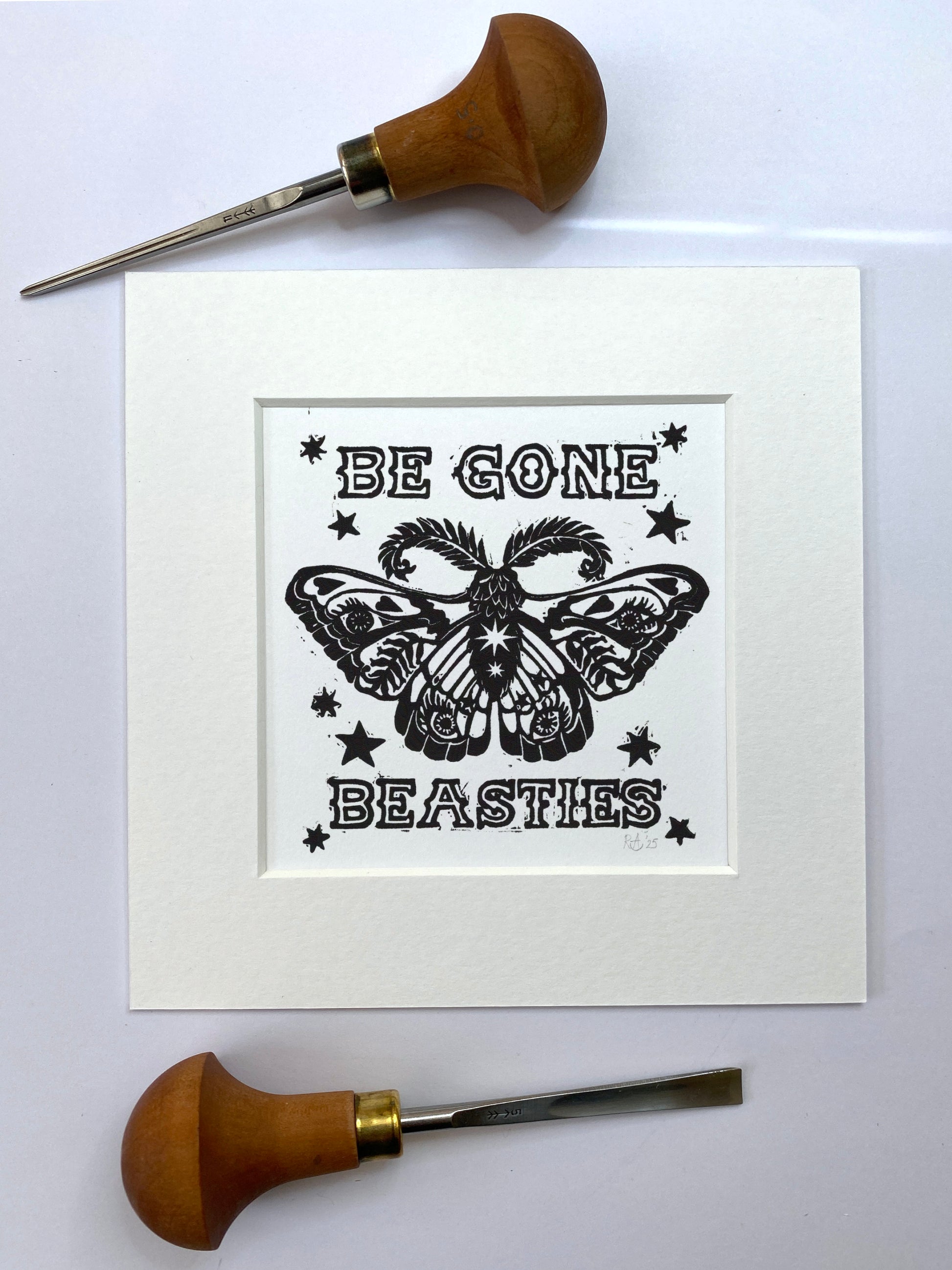 Print with butterfly design and text 'Be Gone Beasties' on a white background, surrounded by woodcarving tools.