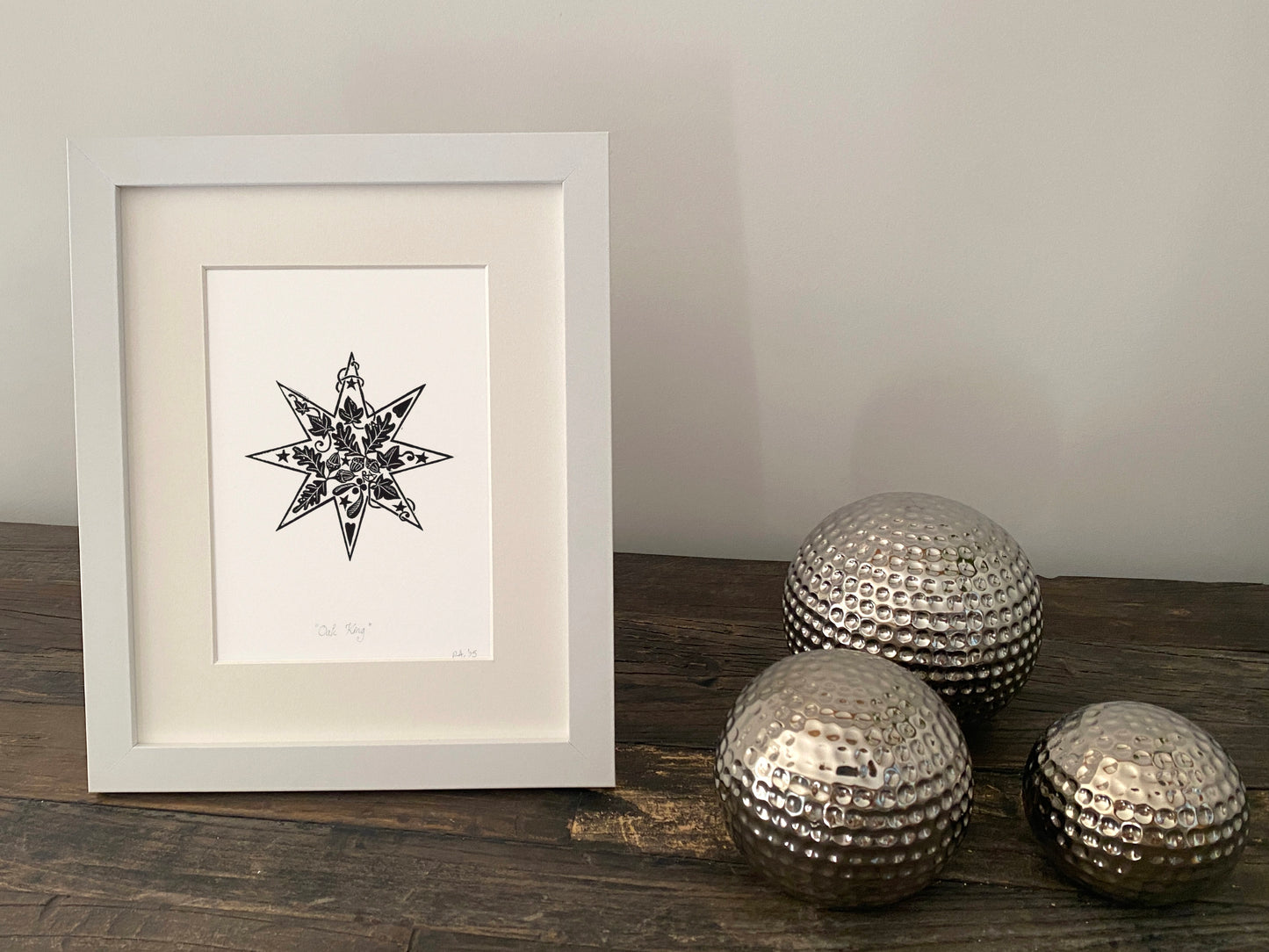Framed artwork with a star design on a wooden surface with decorative metallic balls.