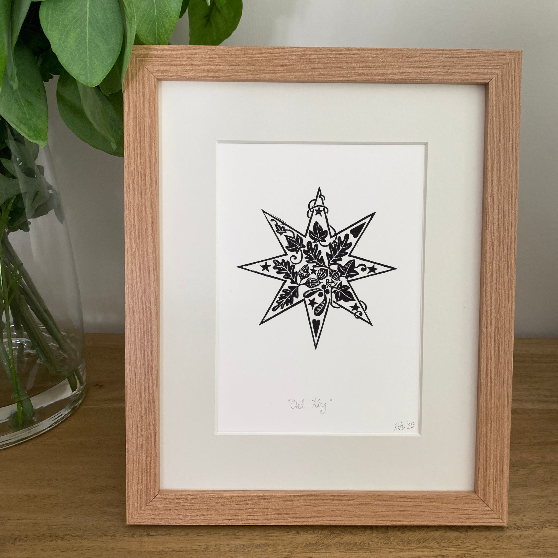Framed black and white star design on a wooden surface with greenery.
