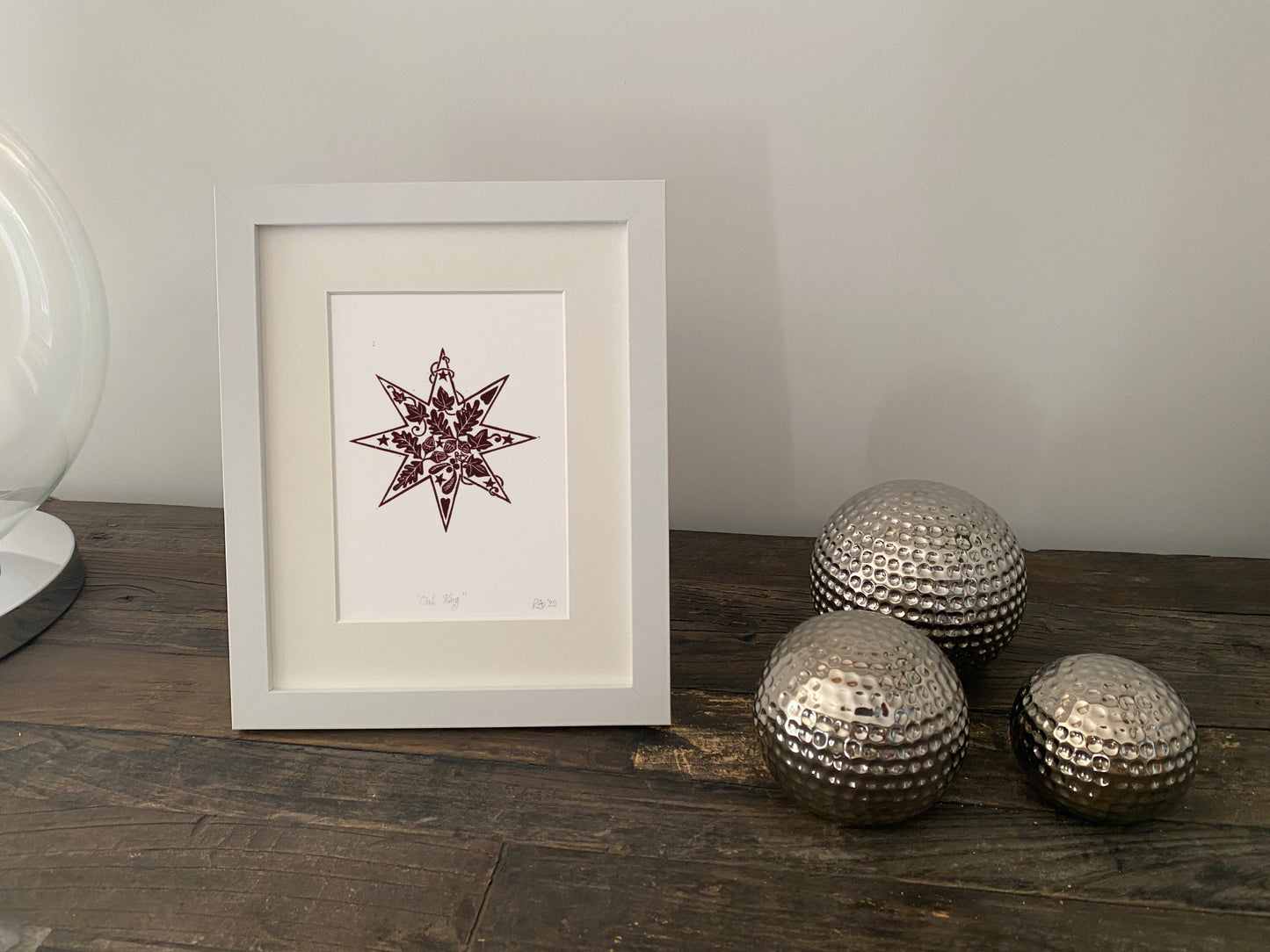 Framed artwork with a star design on a wooden surface next to decorative metallic spheres.
