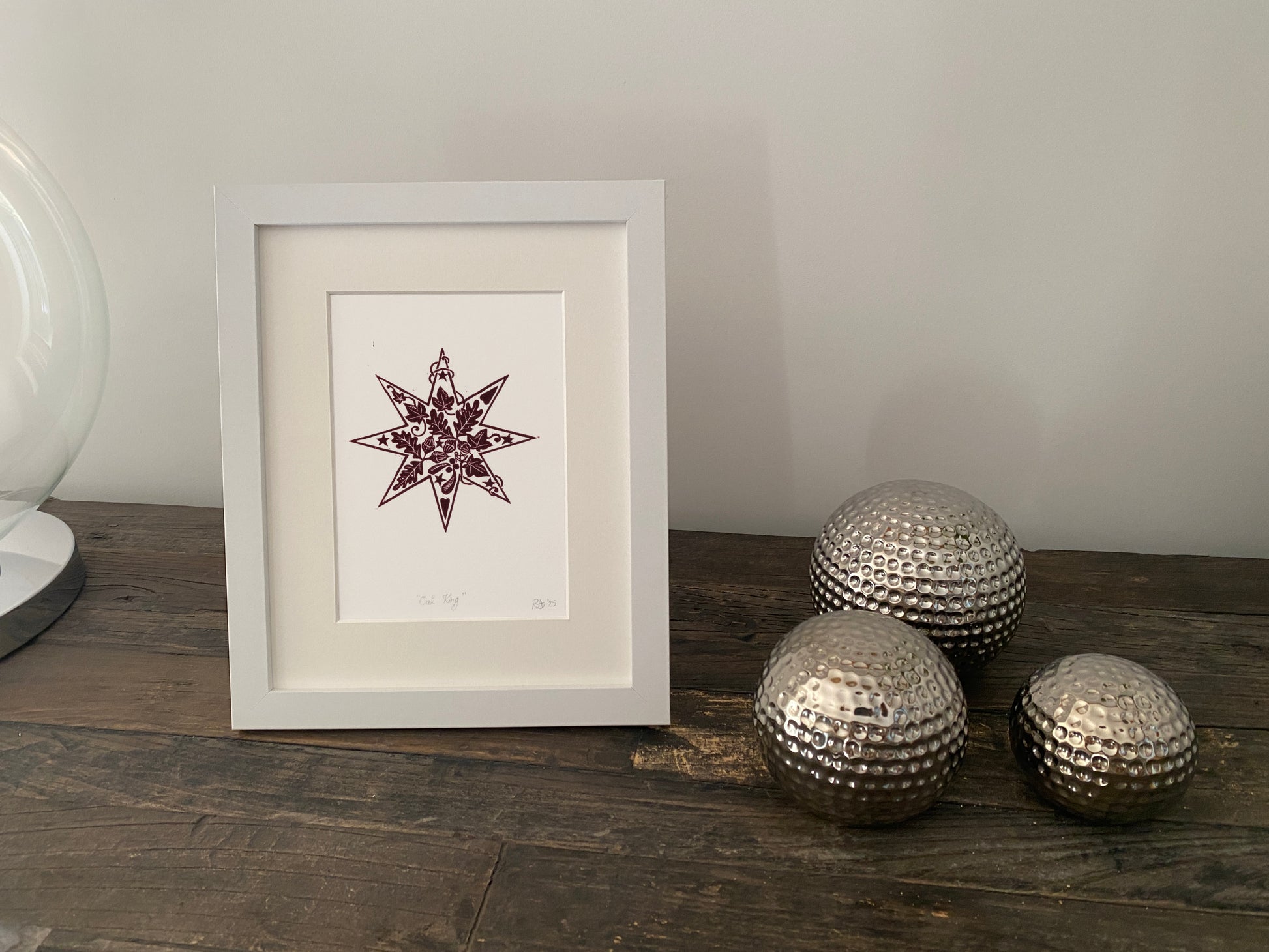 Framed artwork with a star design on a wooden surface next to decorative metallic spheres.