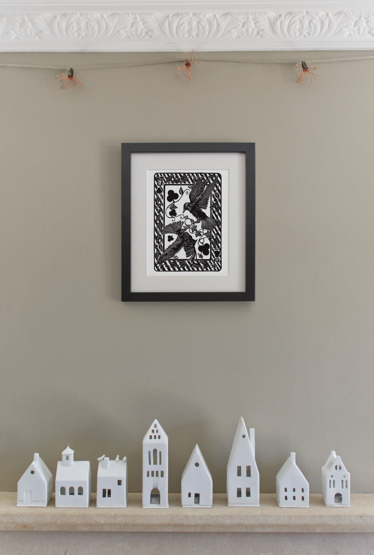 Framed black and white artwork on a wall with small white model houses below.
