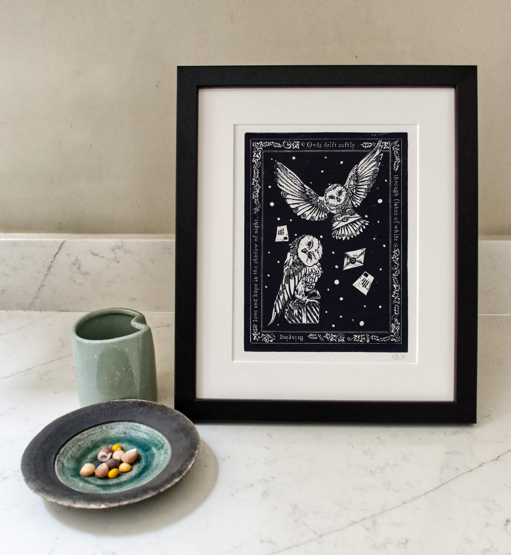 Framed artwork of owls with a celestial design on a white surface with a ceramic cup and plate.
