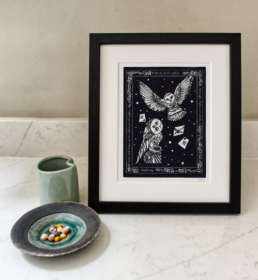 Framed artwork of owls with a celestial design on a white surface with a ceramic cup and plate.