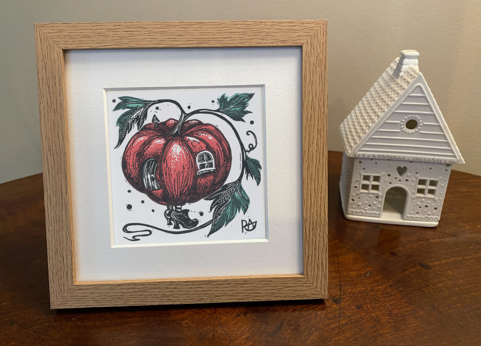 Framed artwork of a pink pumpkin with a house inside on a wooden surface.