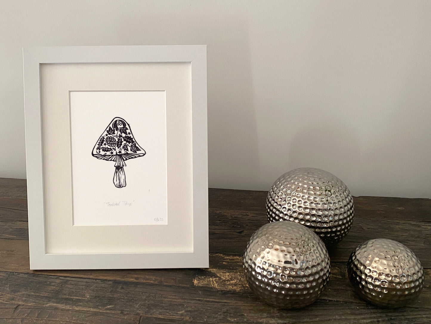 Framed artwork of a mushroom on a wooden surface with decorative metallic spheres.