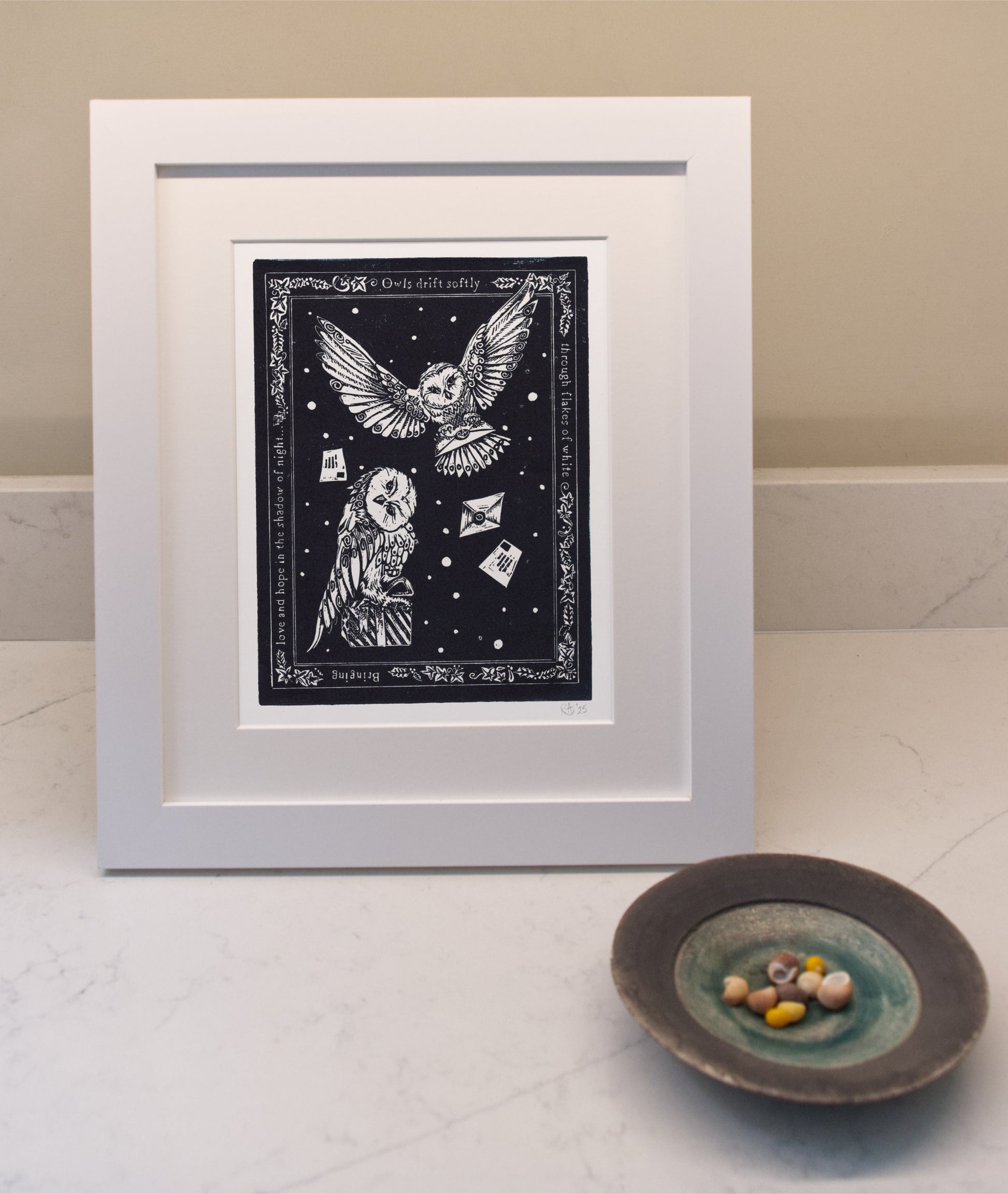 Framed artwork with owls and stars on a white surface with a small dish.