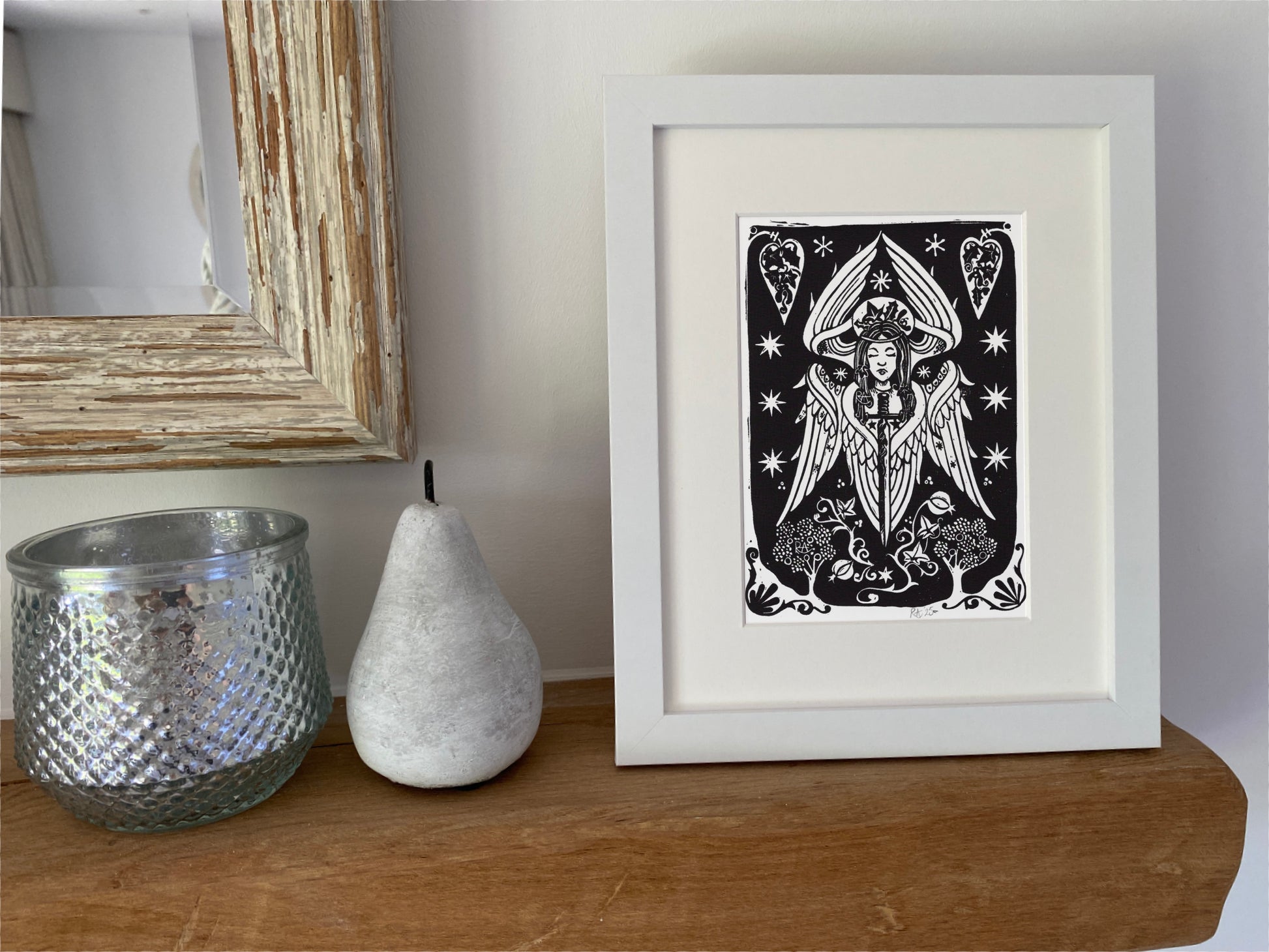 Framed black and white angel artwork on a wooden surface with decorative items.
