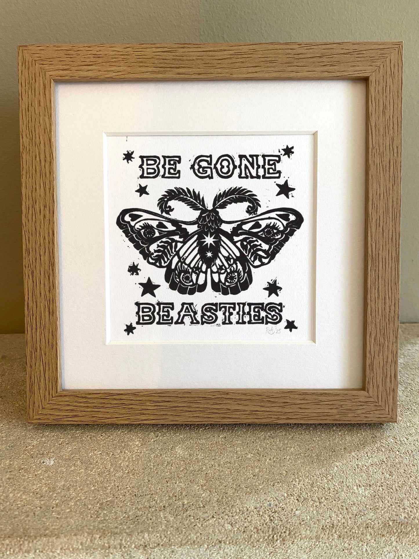 Framed artwork with a black moth design and text 'Be Gone Beasties' on a white background.