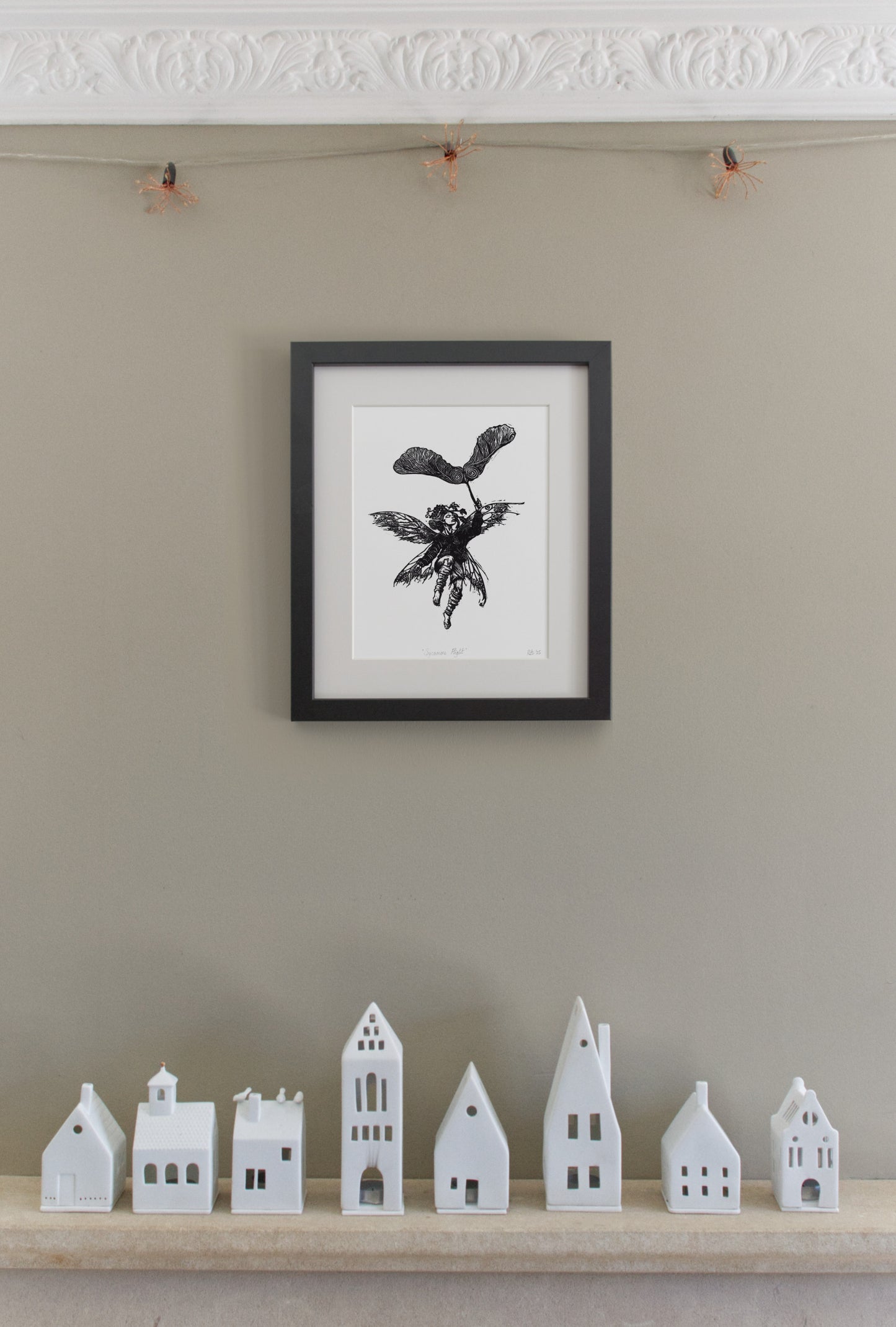 Framed black and white artwork on a beige wall with small white model houses below.