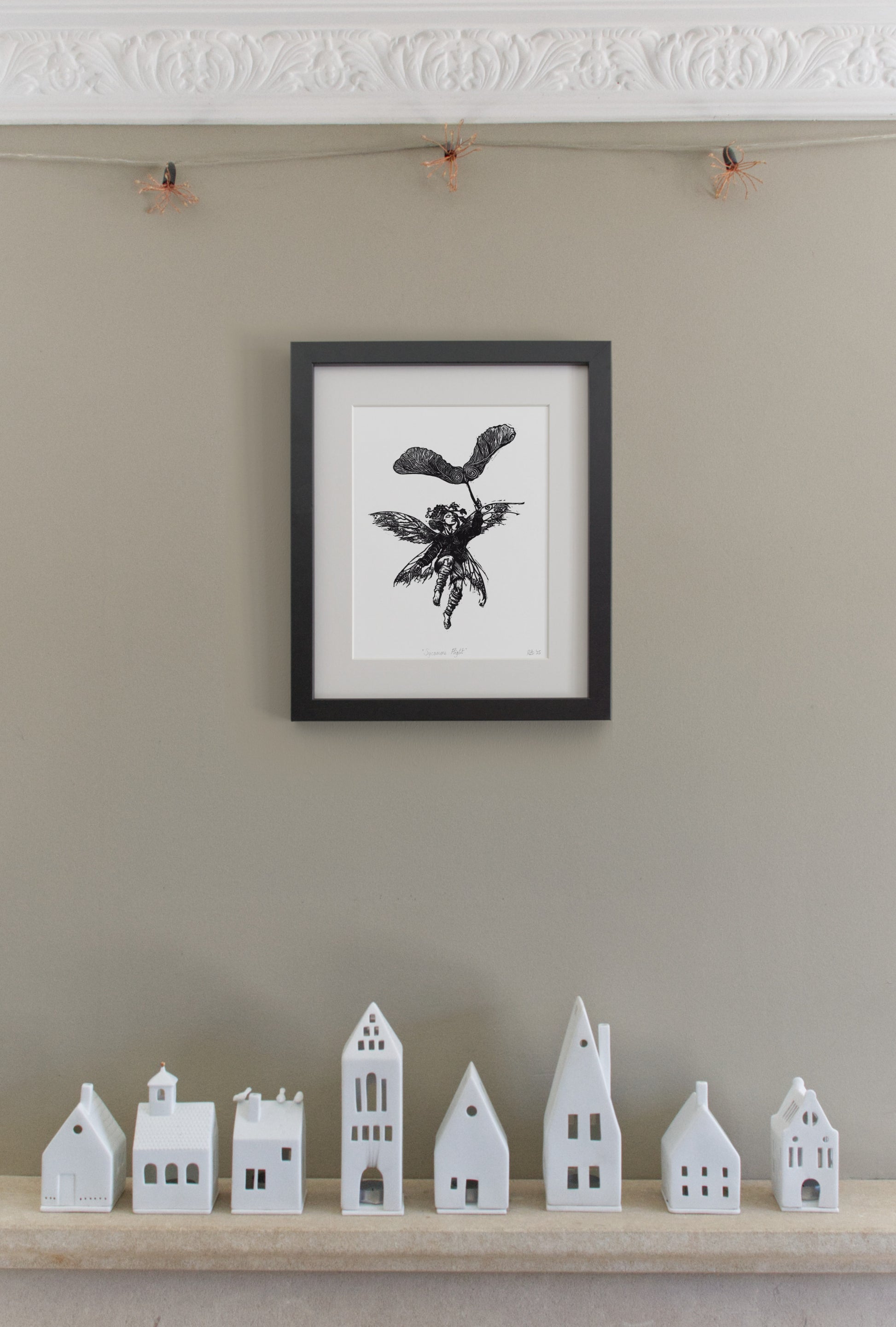 Framed black and white artwork on a beige wall with small white model houses below.